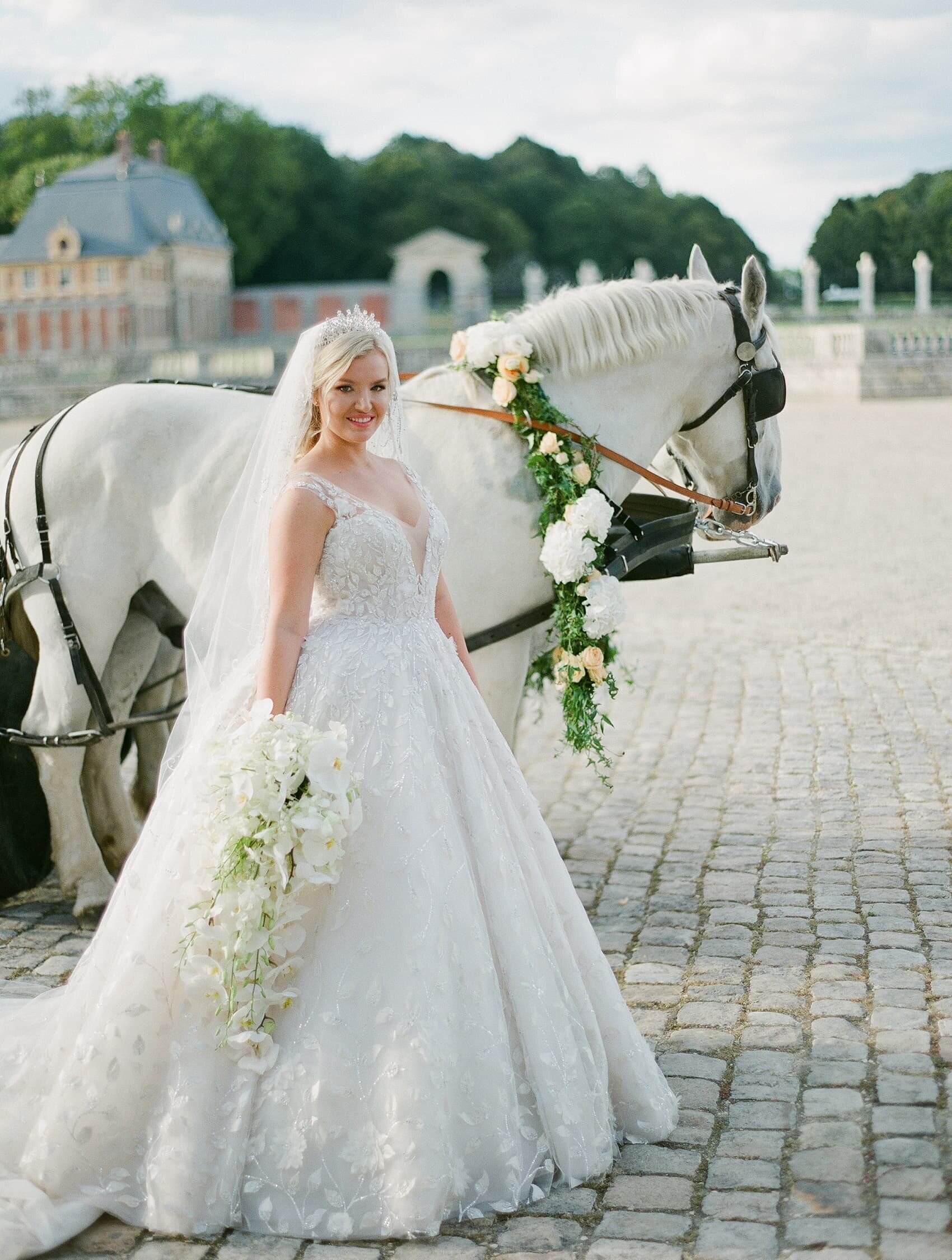 Bride in wedding gown standing next to white horse