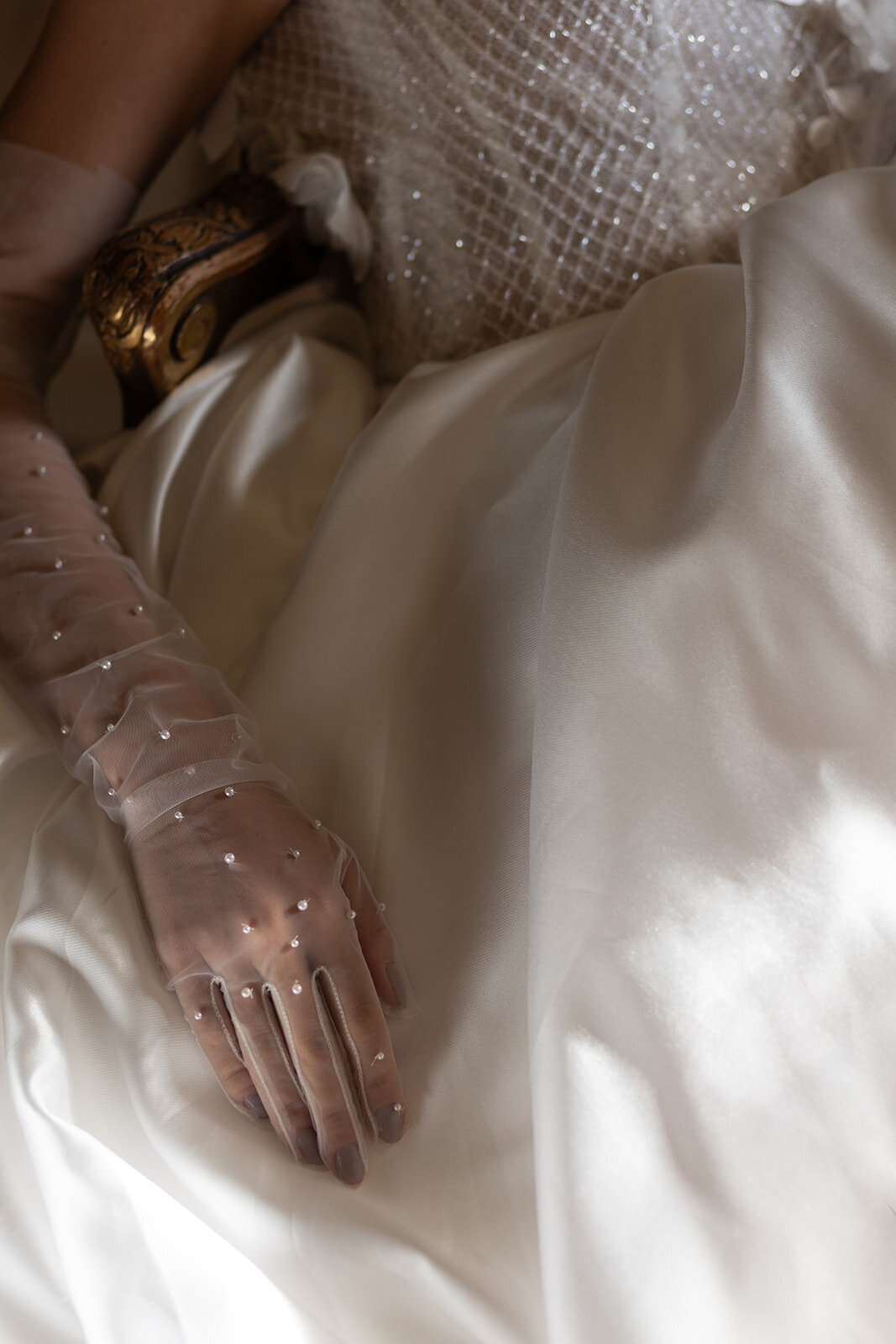 A close-up of a bride’s elegant white gown with sheer pearl-accented gloves, highlighting intricate bridal fashion details.