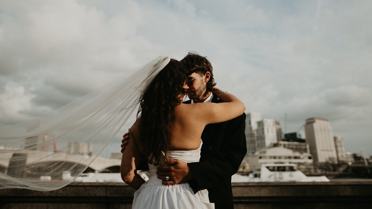 A bride and groom kiss on the Thames in London after their wedding.