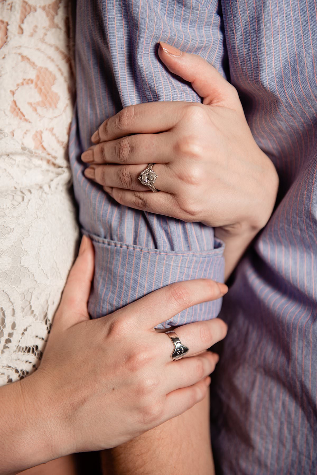 Close up photo of girls hand with engagement ring  as she embraces her fiances arm