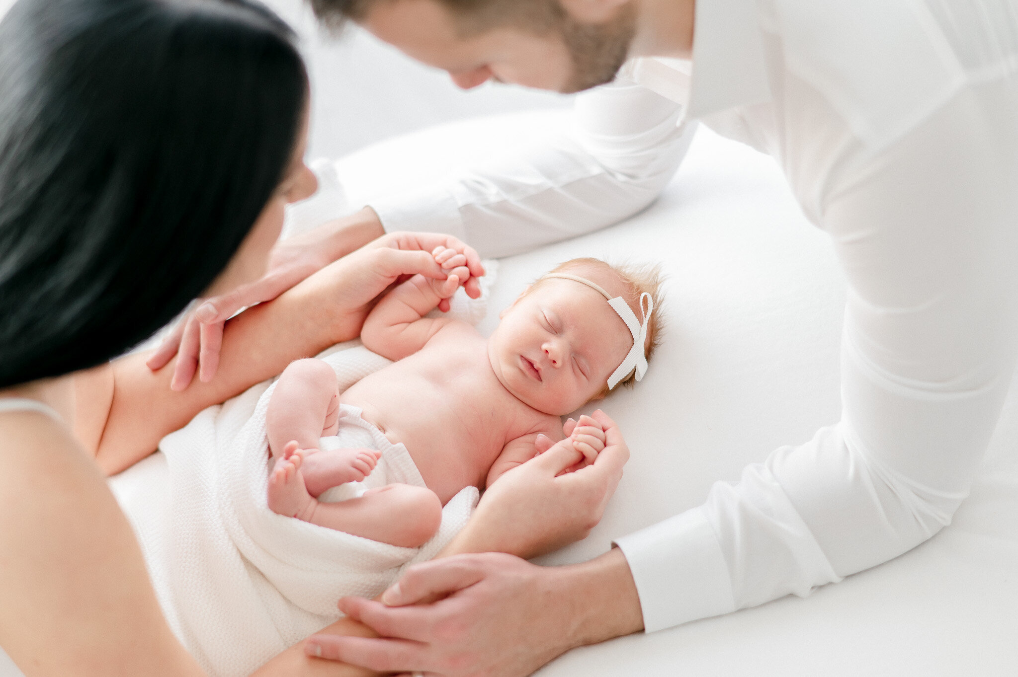A newborn lays on a bean bag with her parent's arms wrapped around her  in Kristie Lloyd's Nashville newborn photography studio