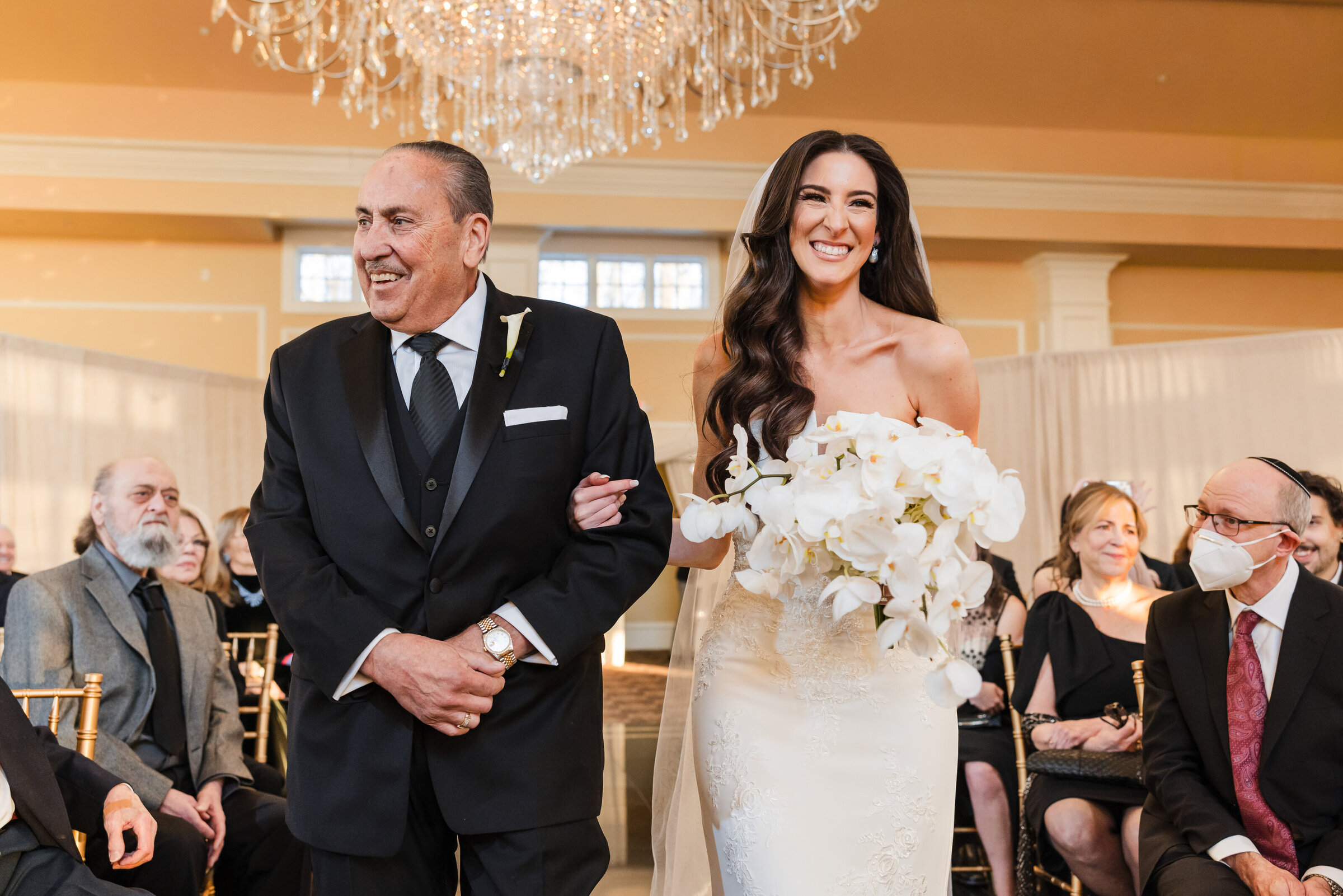 Smily bride holding an orchid bouquet walks down the aisle with her father at Parc Chateau