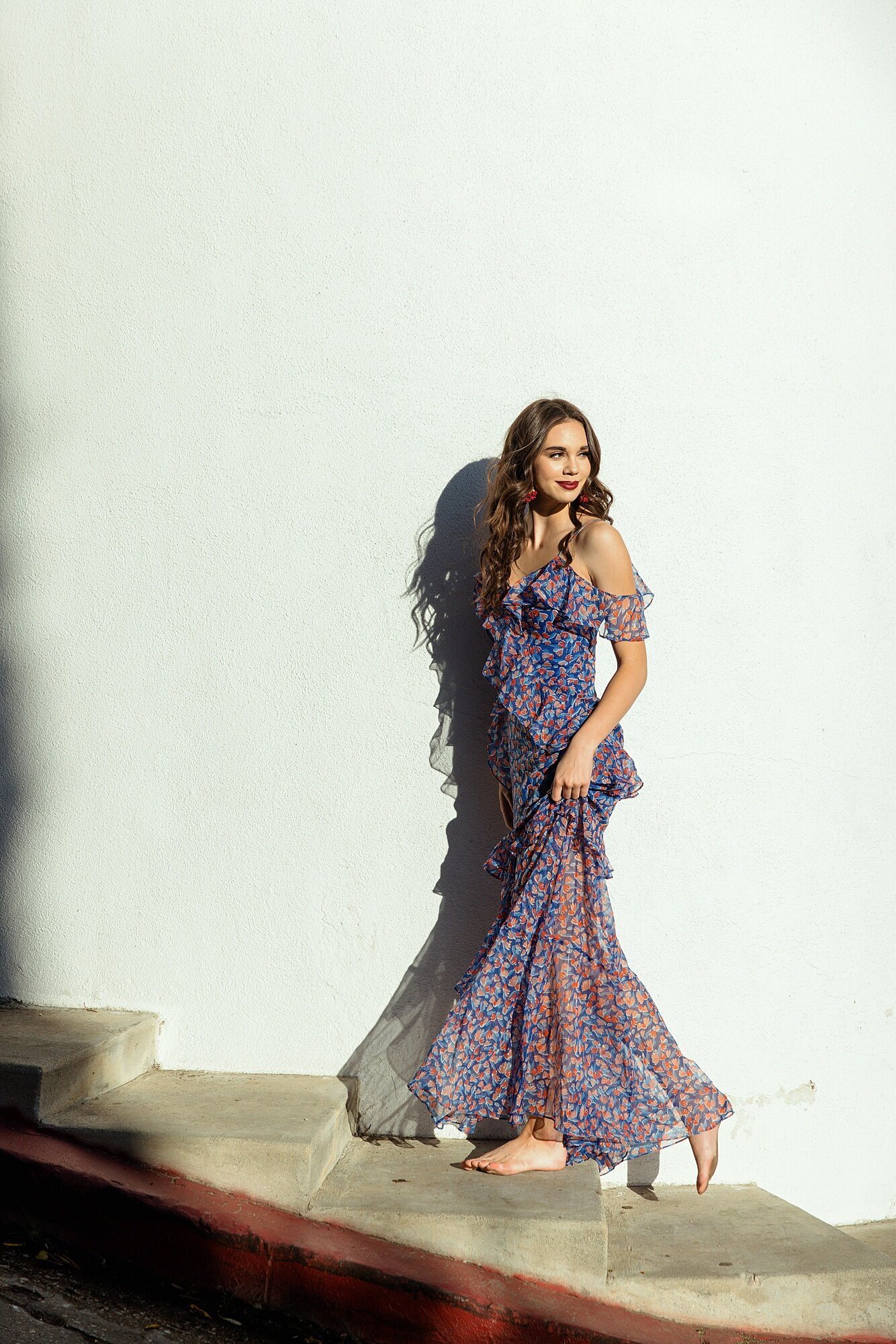 Soft, romantic portrait of a woman in a white flowy dress with boho-chic earrings, against a light colored wall.