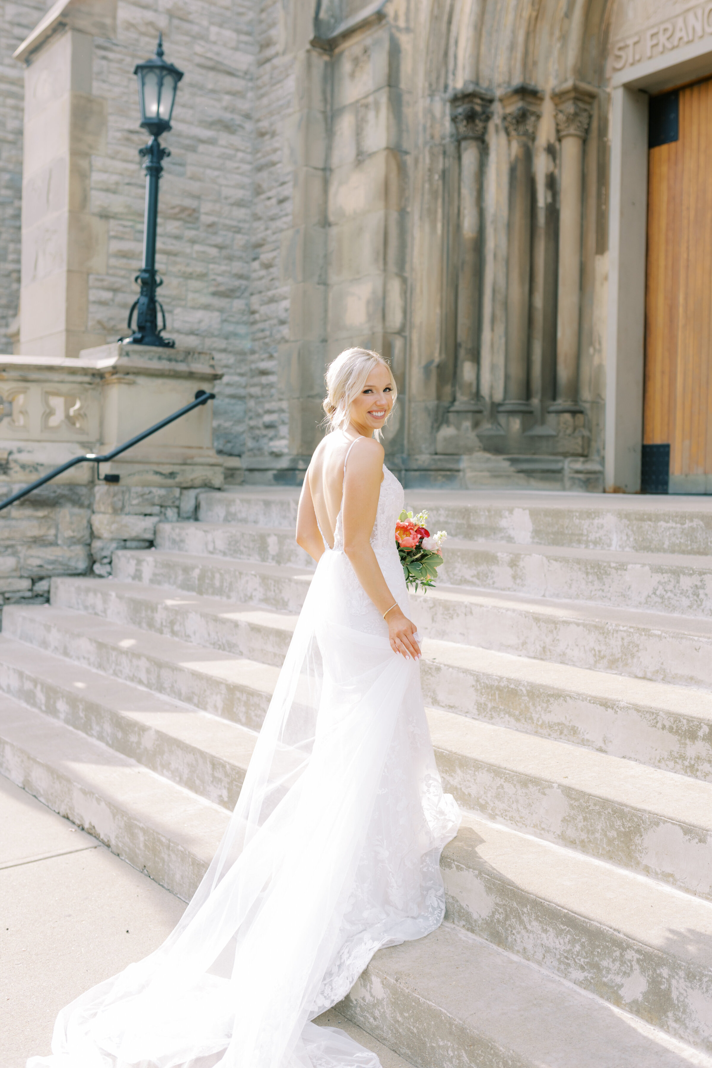 Bride walking up the stairs into the church on her wedding day smiling towards the camera