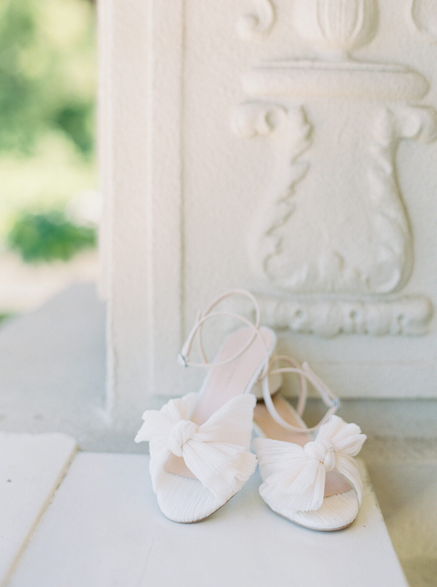 white bow bridal shoes against white stucco historic building