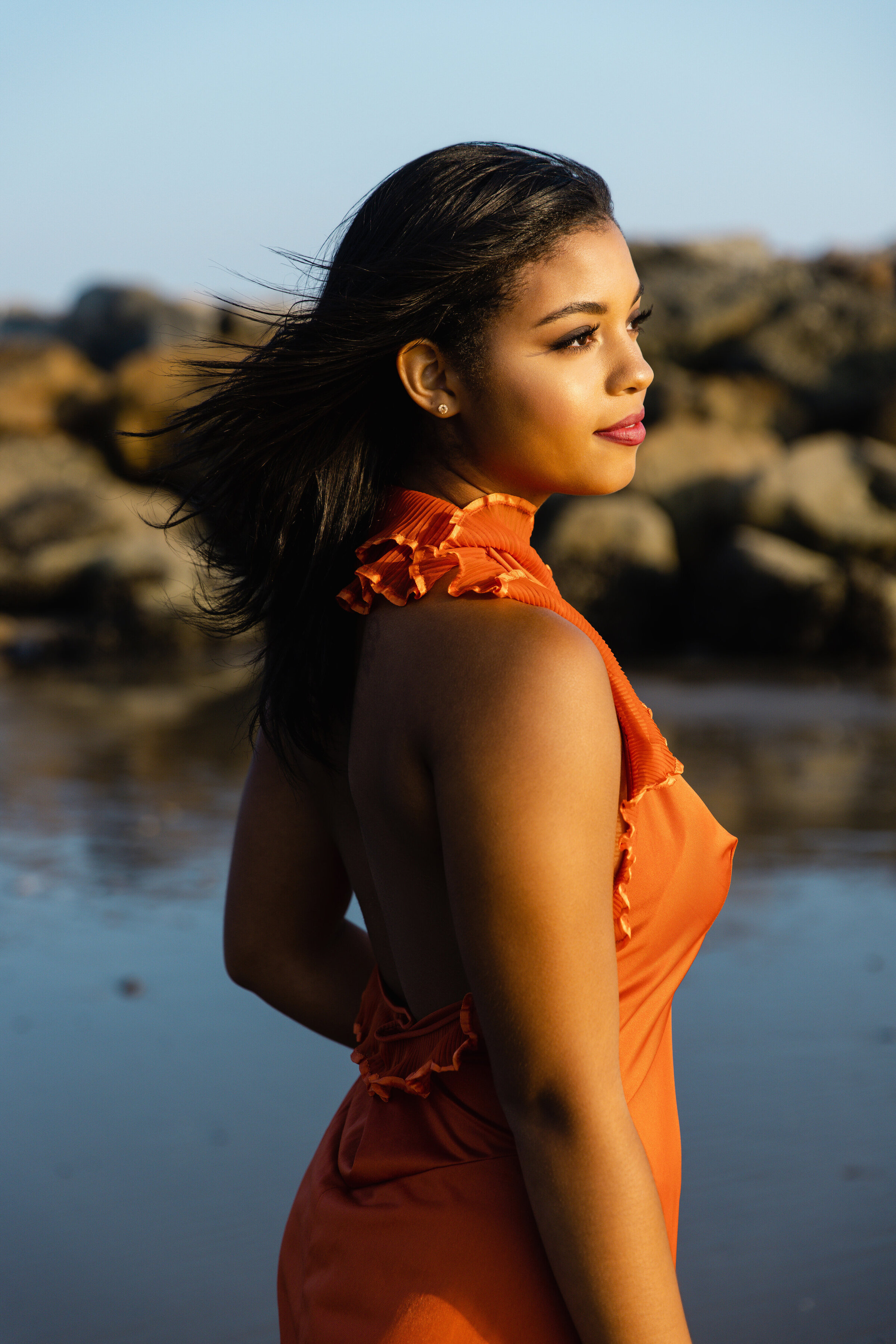 Editorial senior portrait of a high school girl in an orange dress standing on the beach during golden hour, photographed by Los Angeles senior photographer Tara Rochelle.
