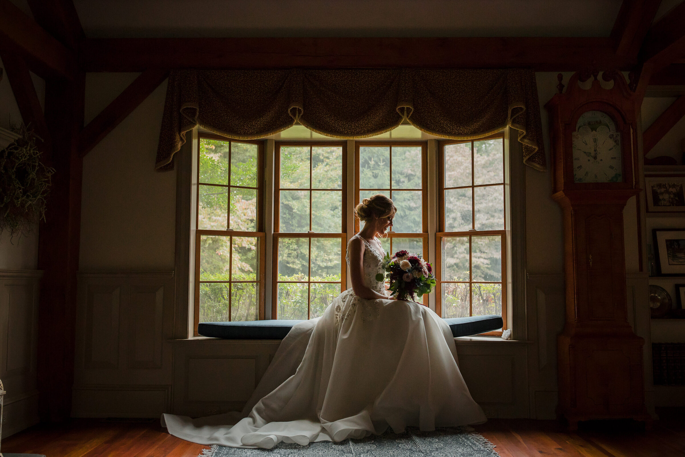 Bride in a puffy dress sitting by the window looking at her bouquet at French Creek Golf Club