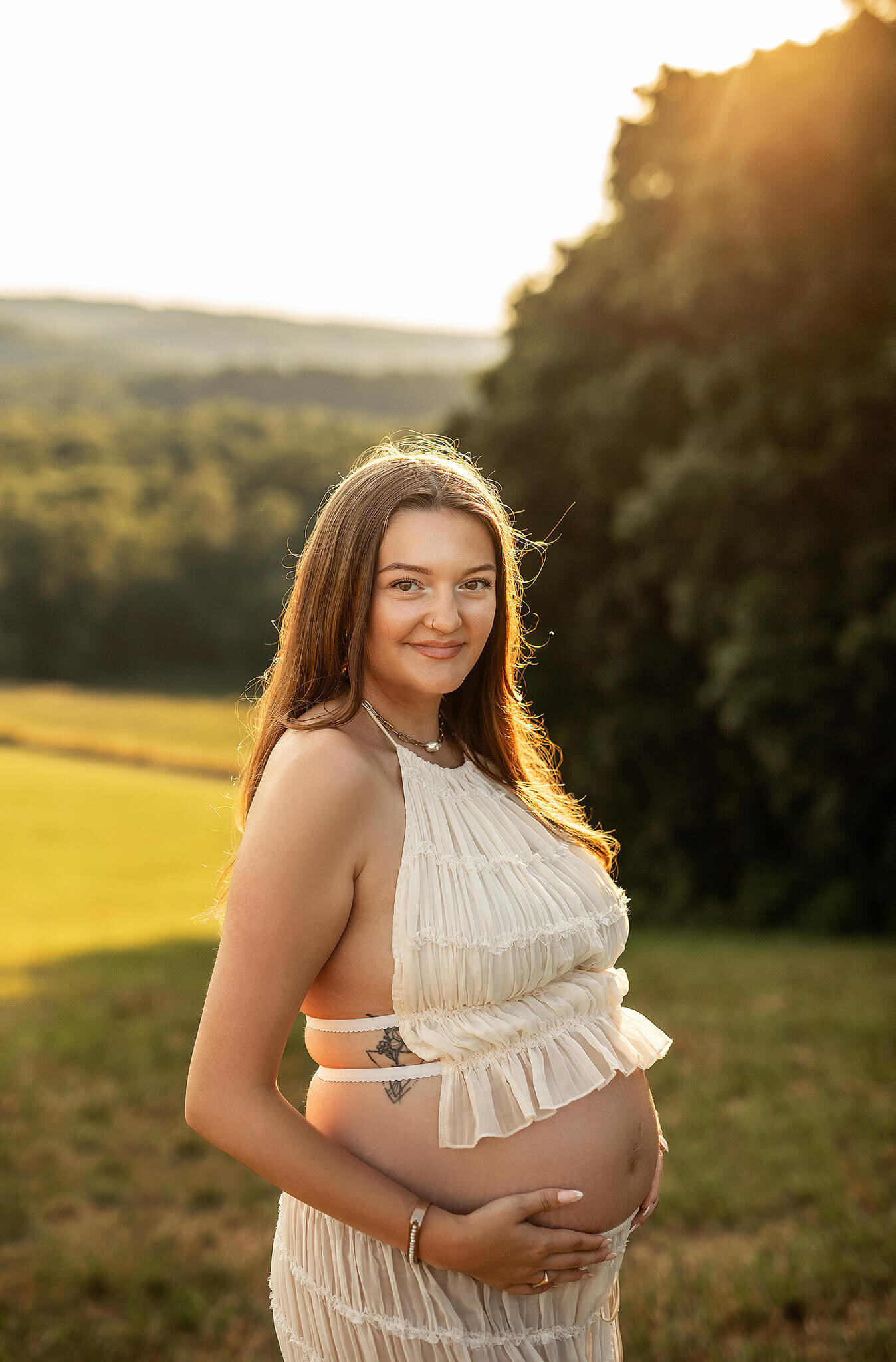 Maternity photo of mama standing on a tall hill with her belly showing and sunlight behind her