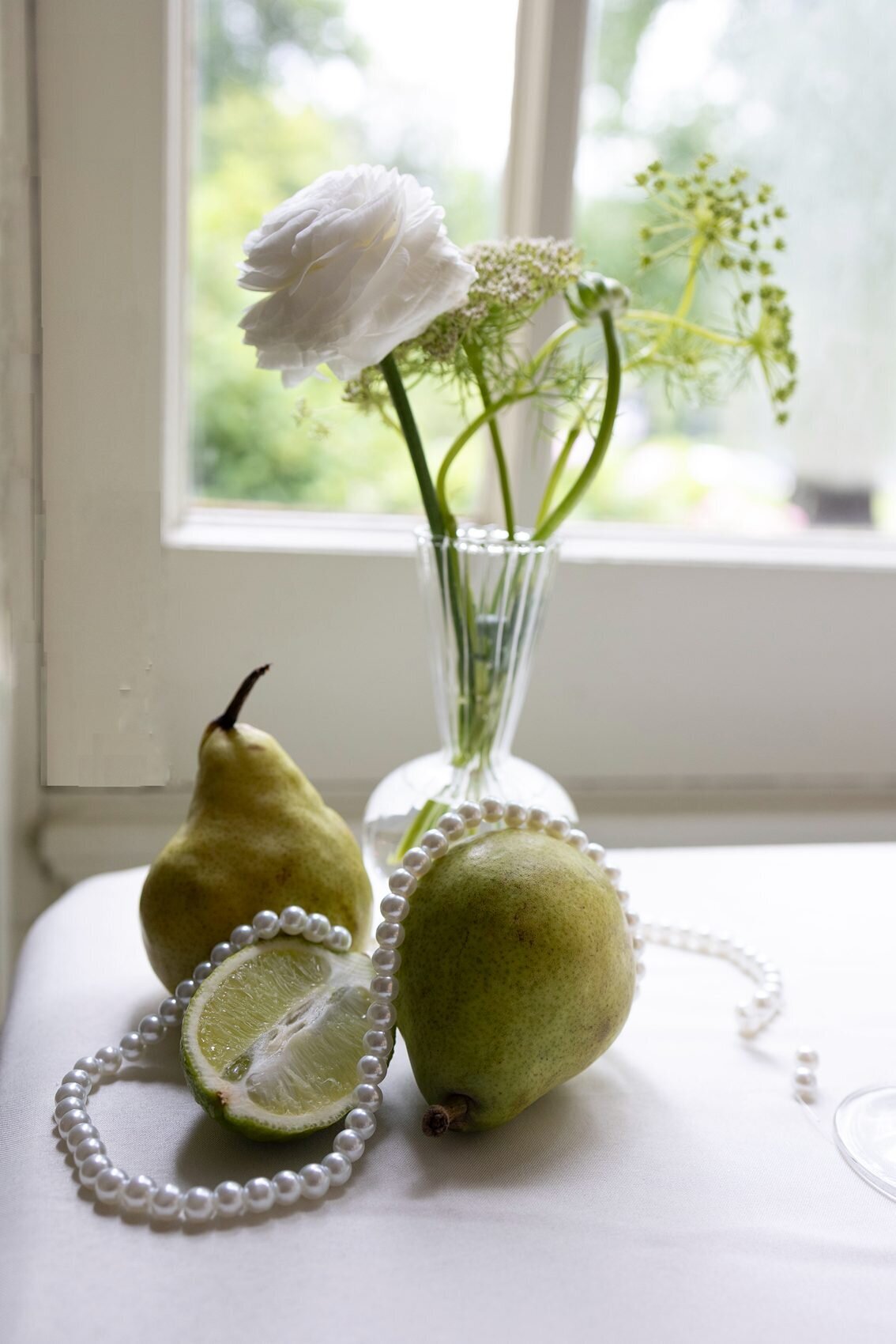 Vignette of green apples and a lime adorned with pearls next to a small vase with white flowers at an escort table.