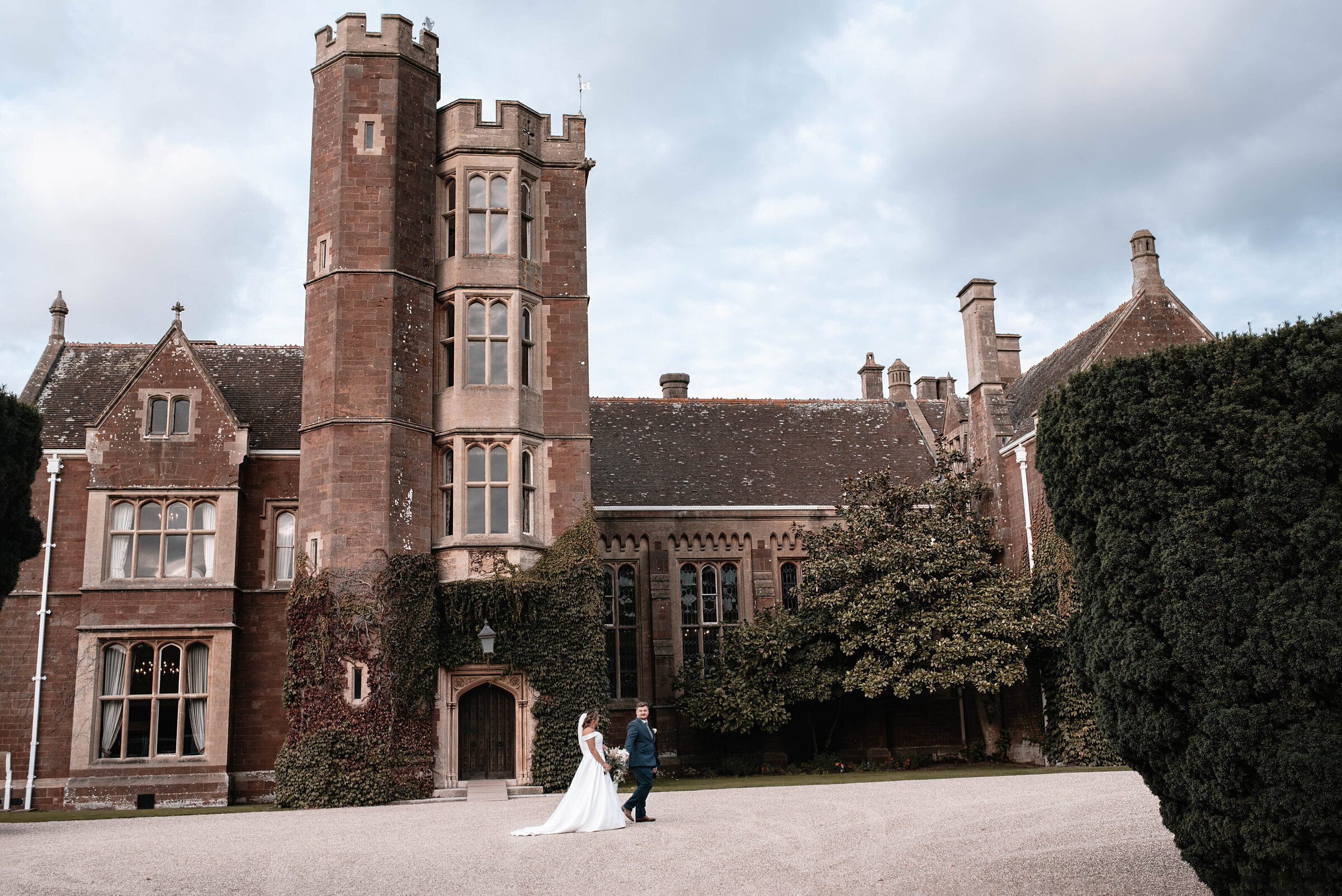 Bride and Groom walking across the driveway outside St Audries Park wedding venue in Somerset