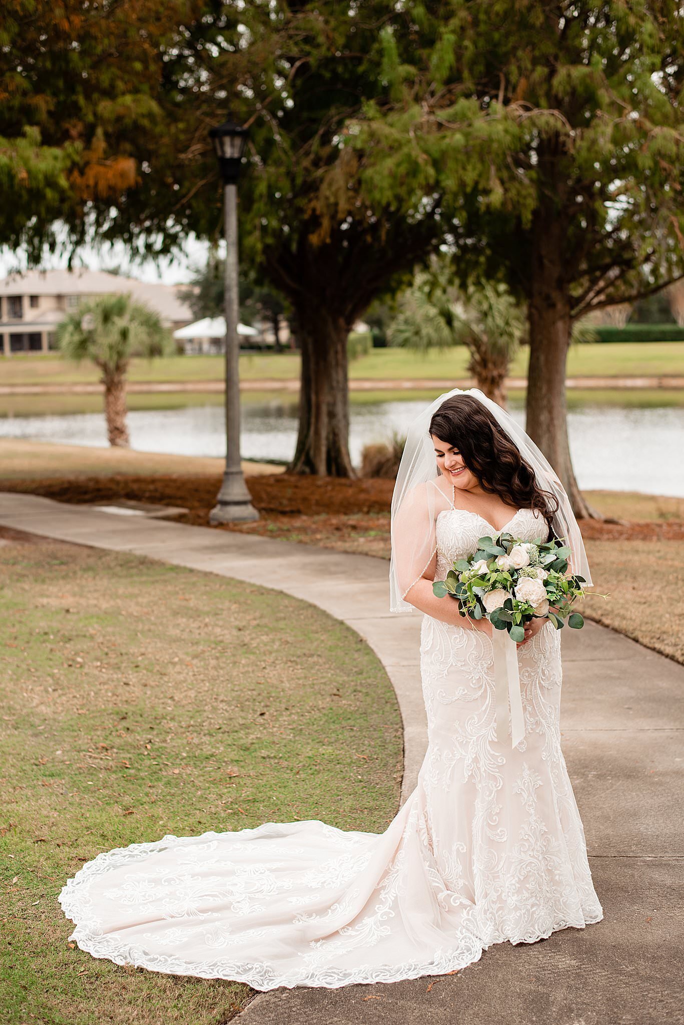 Bride holding her bouquet wearing a sweetheart dress and looking down at her train, palm trees in the back and a pond beside her