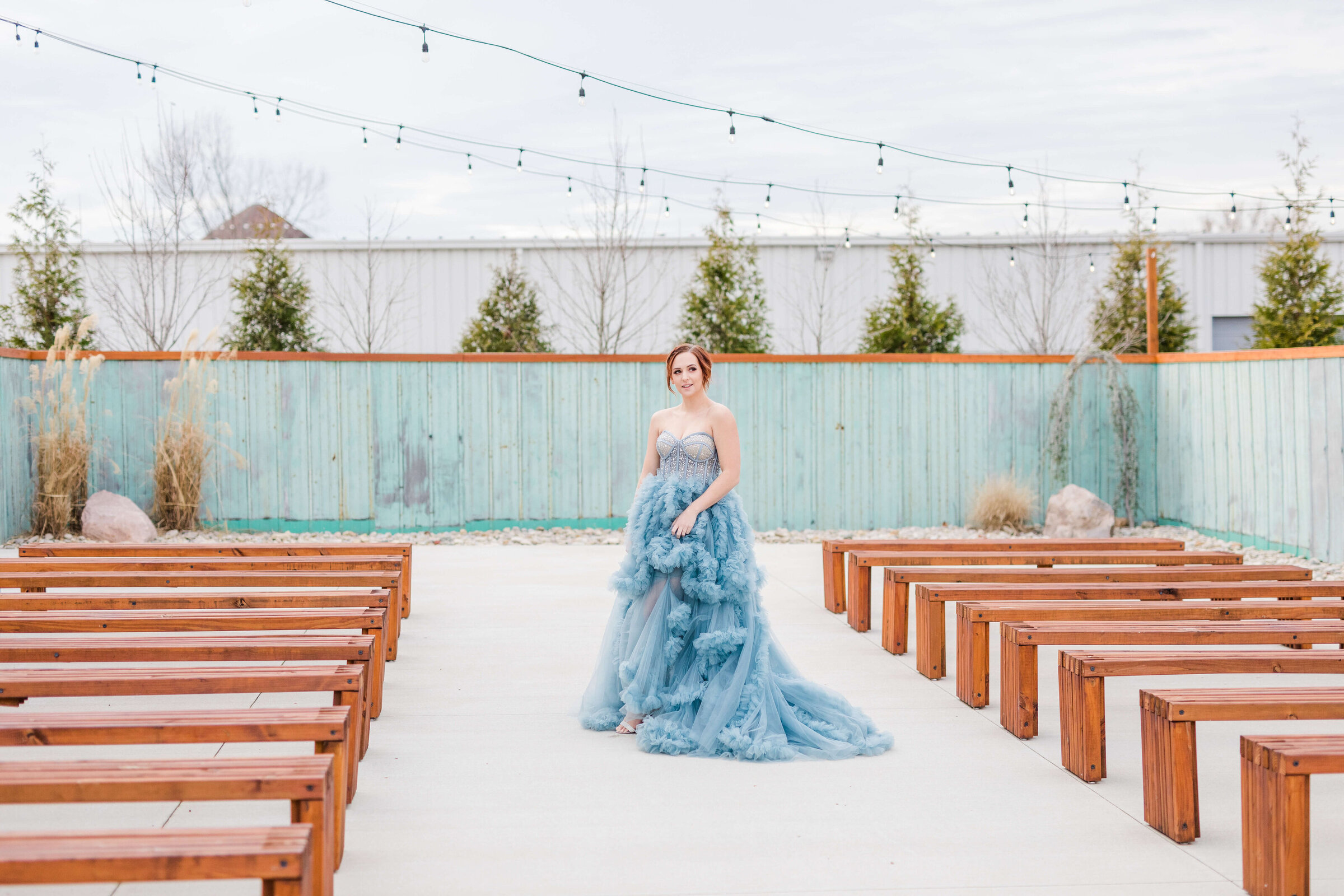 A bride in a blue dress stands in between the ceremony pews at mojave east