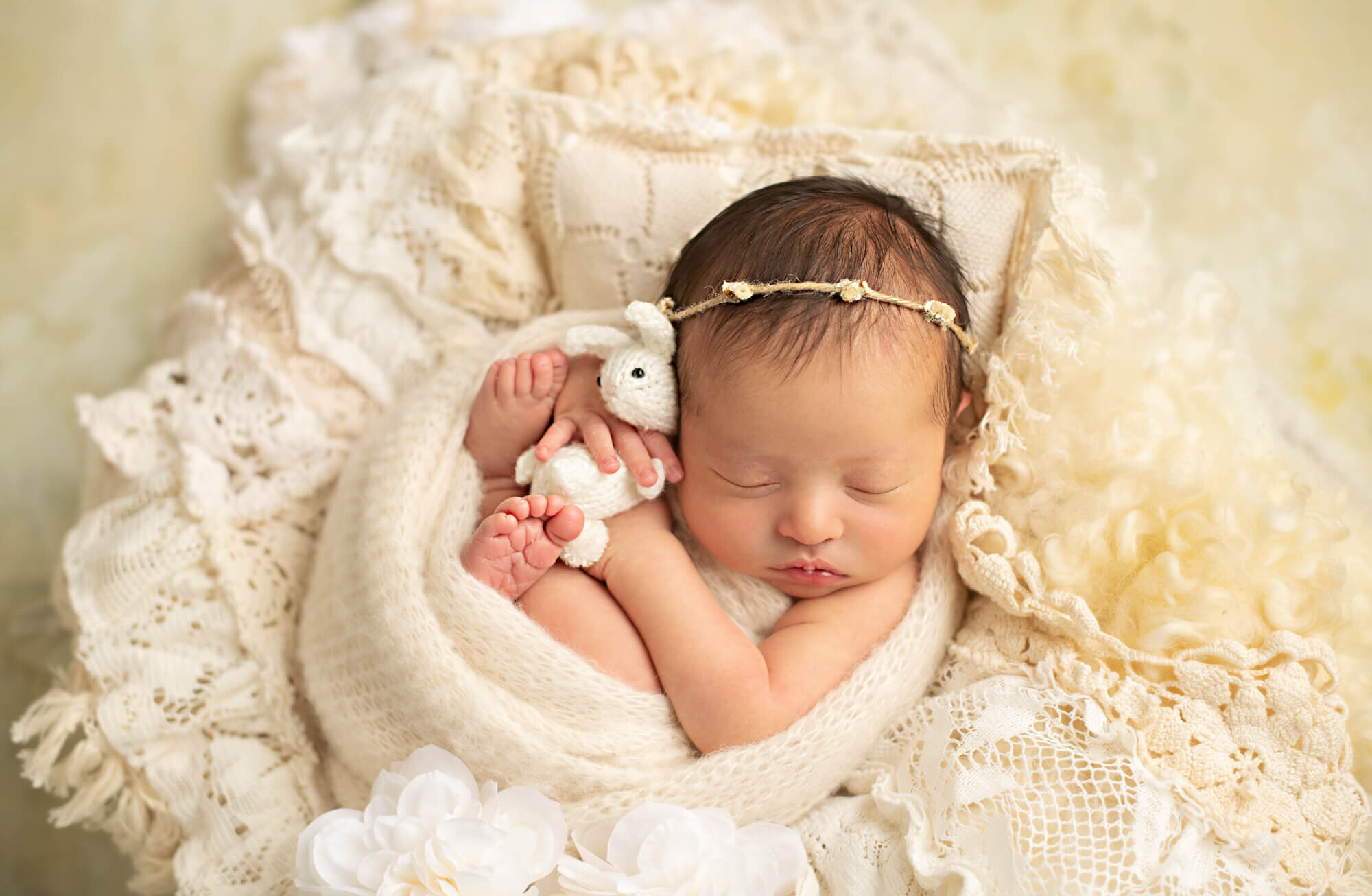 Sleeping newborn girl in sweater wrap with stuffed cuddle bunny
