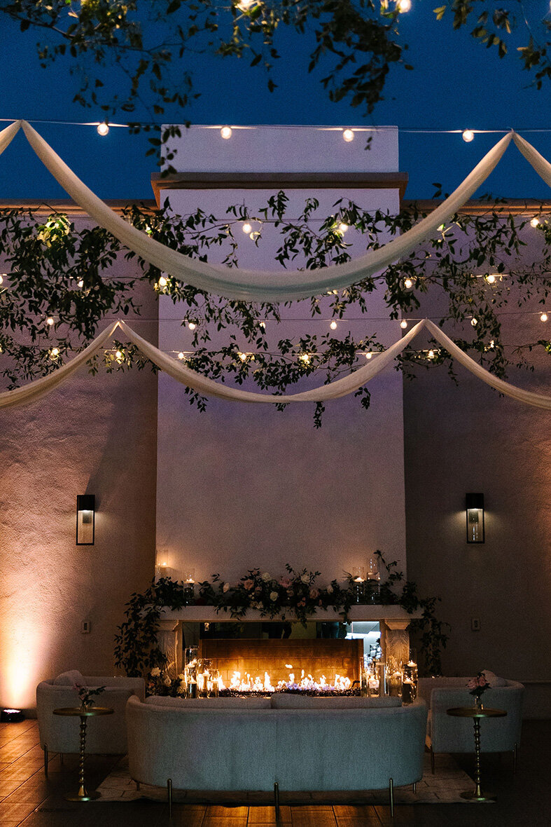 The outdoor fireplace at SoHo63, a Chandler wedding and event venue, glows beneath romantic drapery, hanging greenery, and twinkle lights. This evening setup creates a magical backdrop for wedding ceremonies or receptions in the heart of downtown Chandler.
