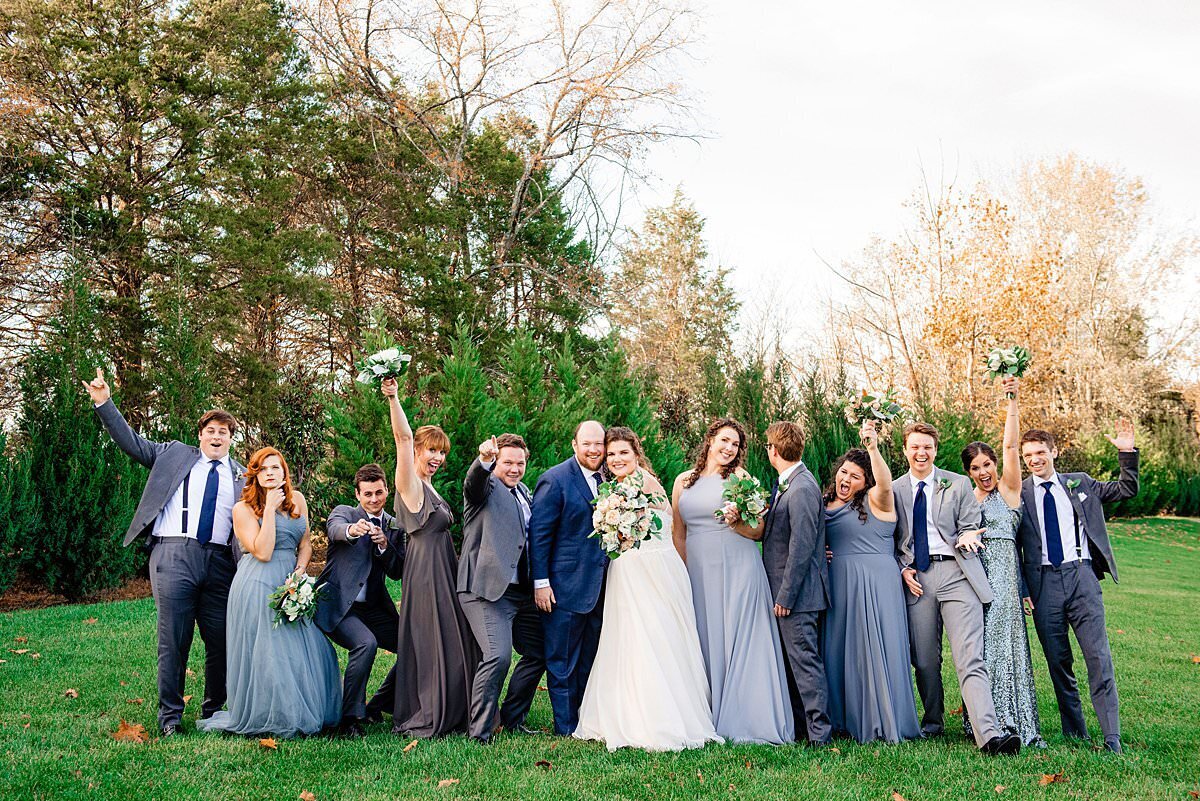 Wedding party wearing shades of blue and grey having fun during photos at Sycamore Farms