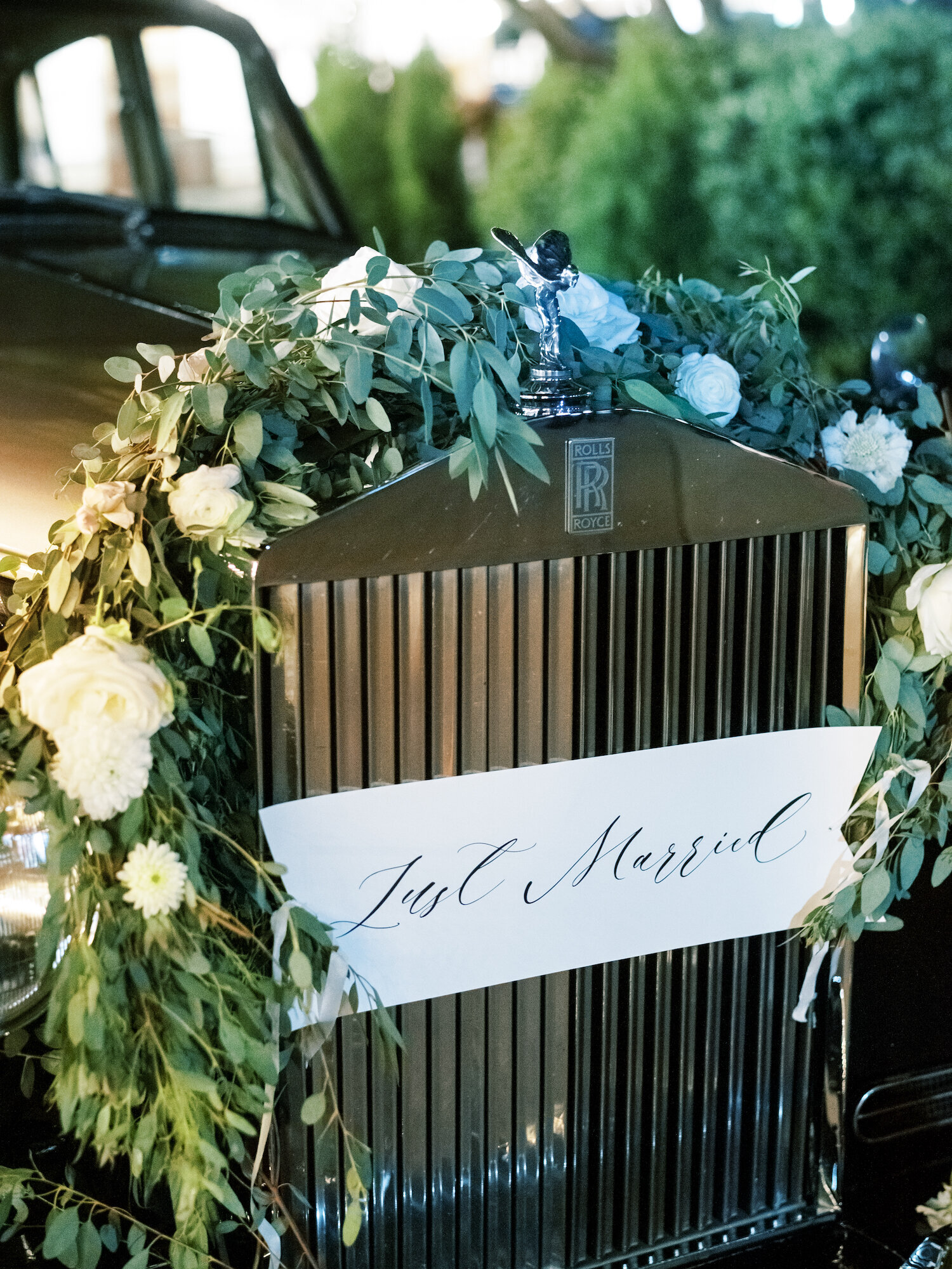 rolls royce decorated with green and white florals for wedding getaway car