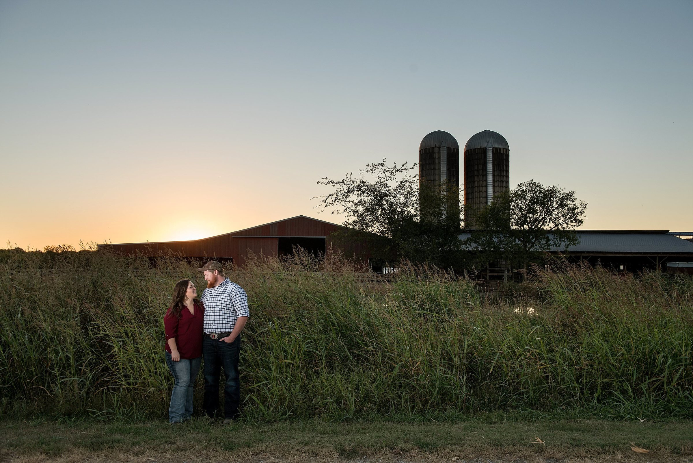 Couple standing together on family land with the family farm in the background showing 2 grain silos