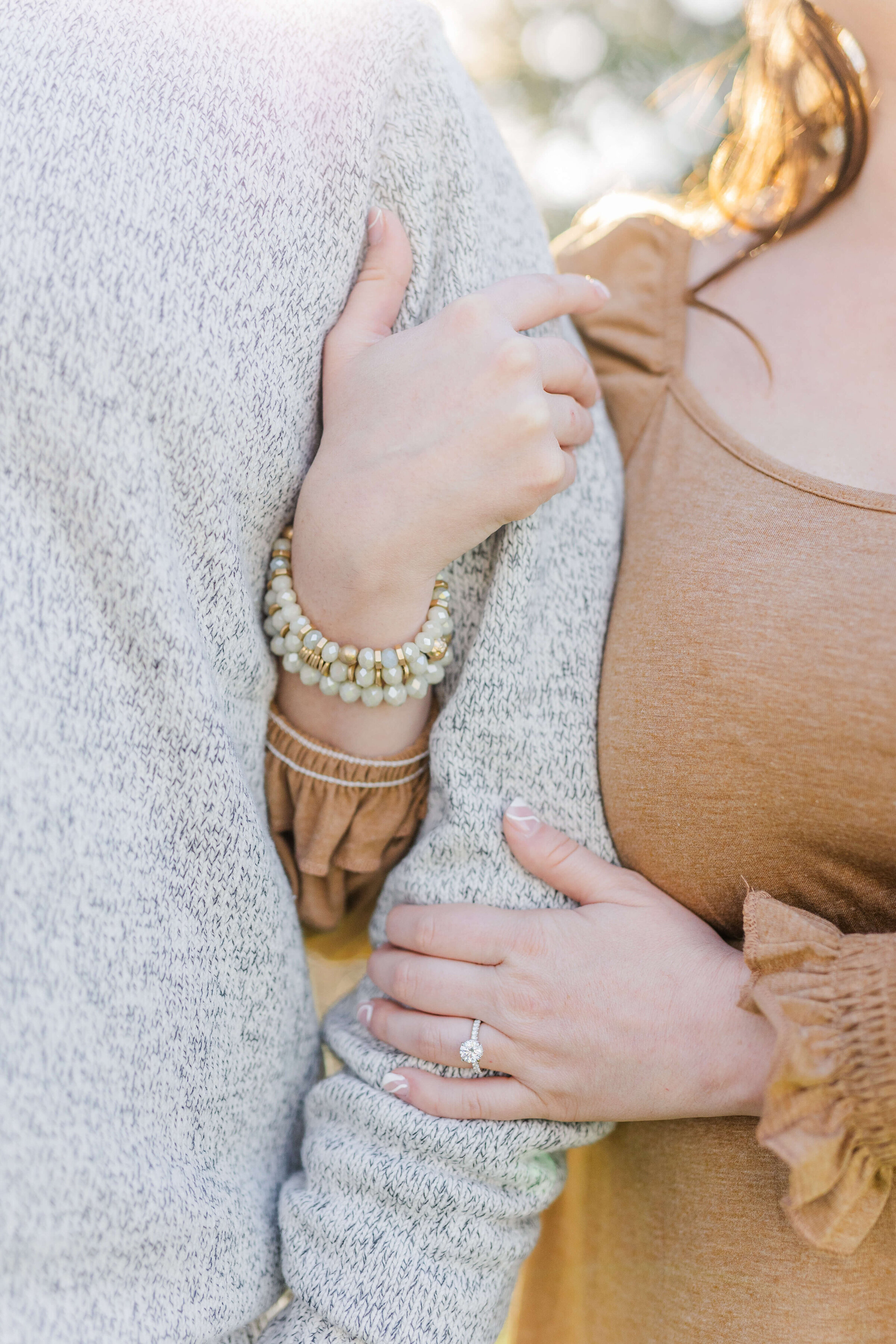 A close up photograph of a man and woman's arms interlinked with one another and a close up of her engagement ring
