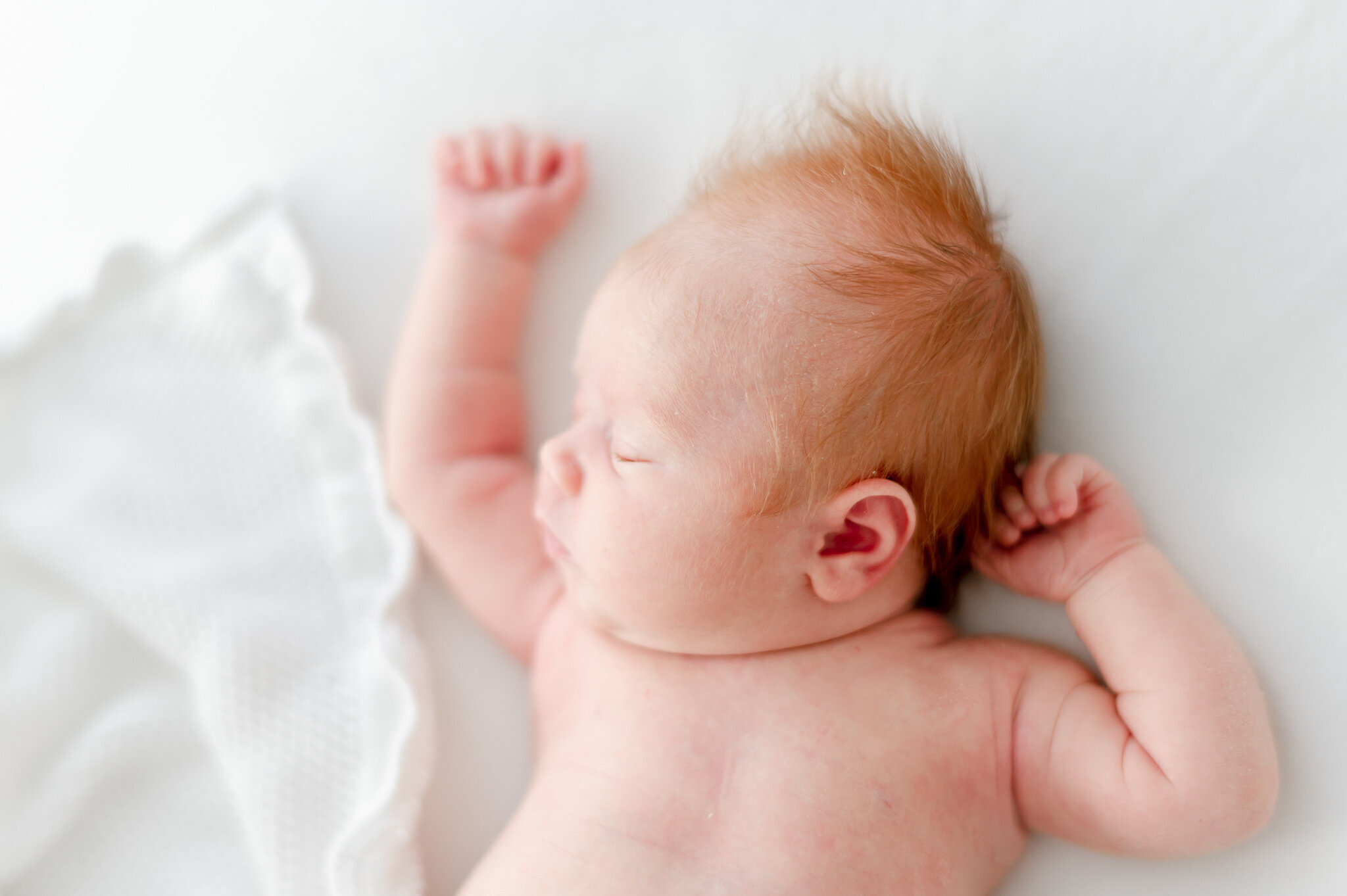 Red haired newborn sleeps on a white bean bag  in Kristie Lloyd's Nashville newborn photography studio
