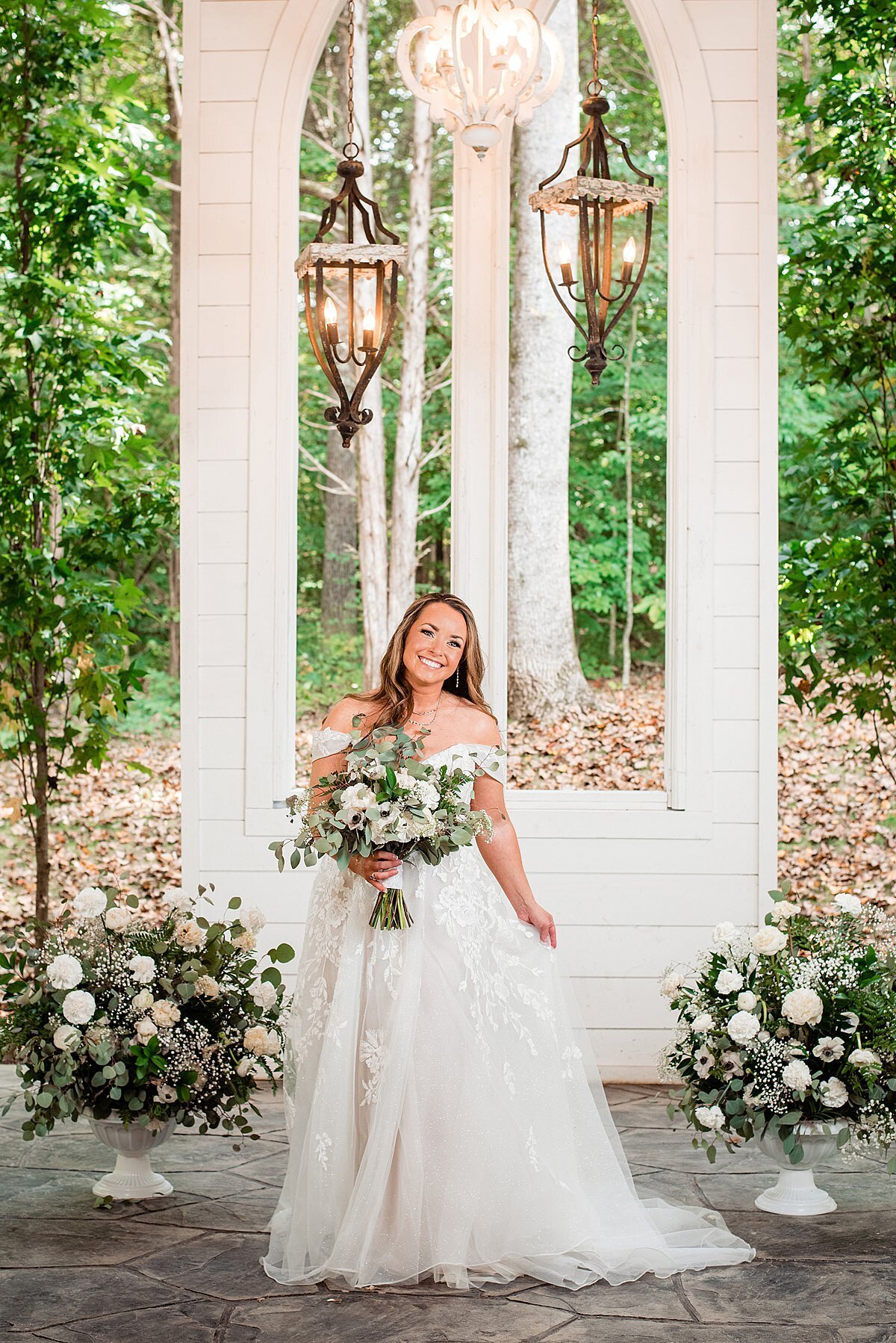 Bride standing beside large flower arrnagements underneath lanterns in the open air church at Firefly Lane
