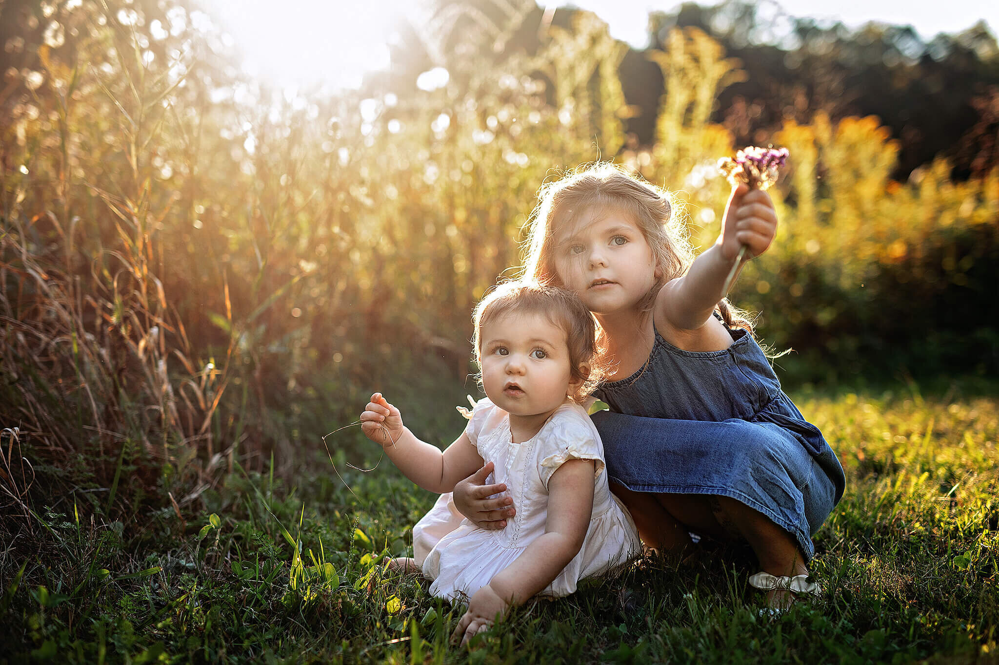 Sisters sitting on the ground together with beautiful light behind them