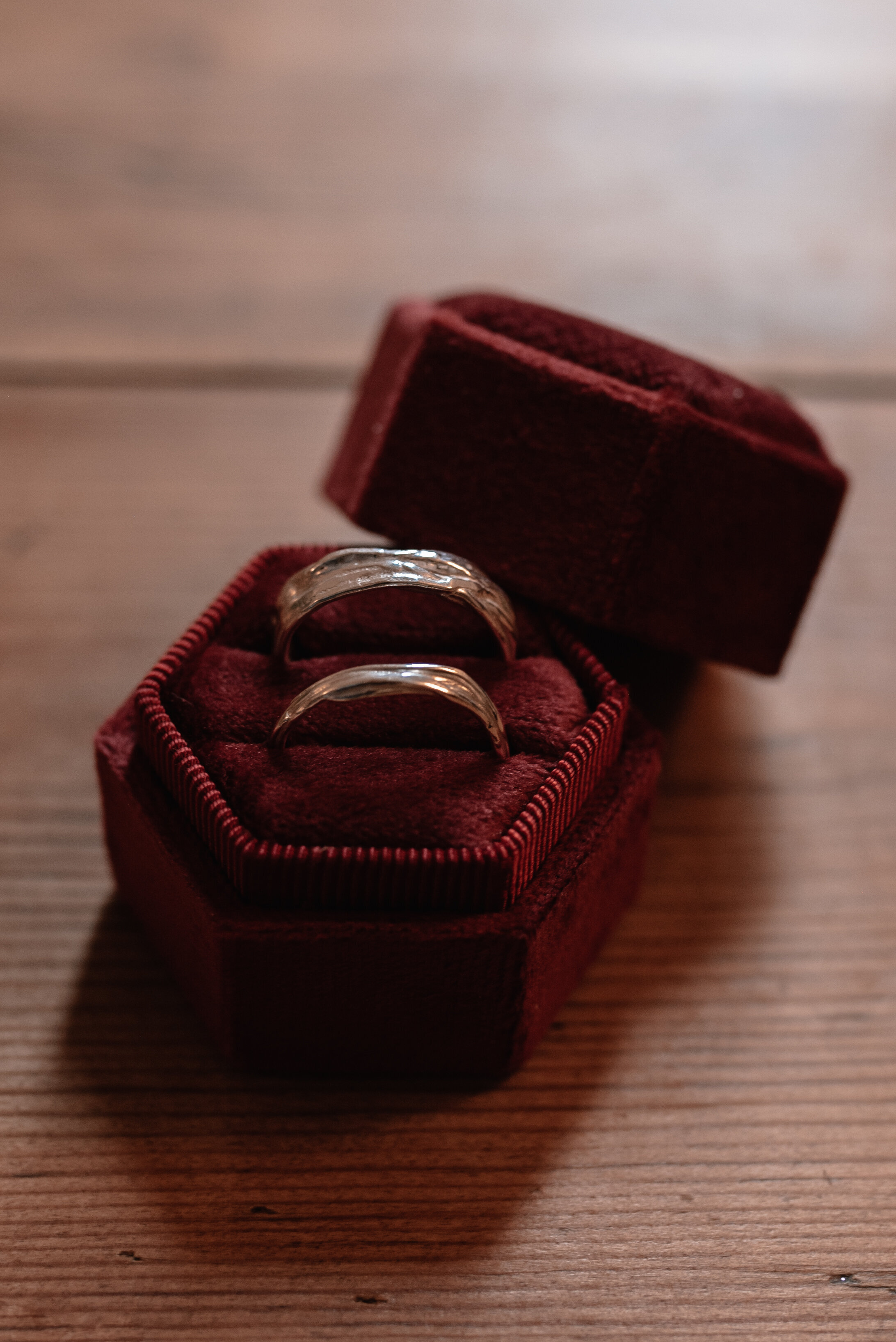 Hand crafted wedding rings seated in a red velvet ring box on top of a wooden table