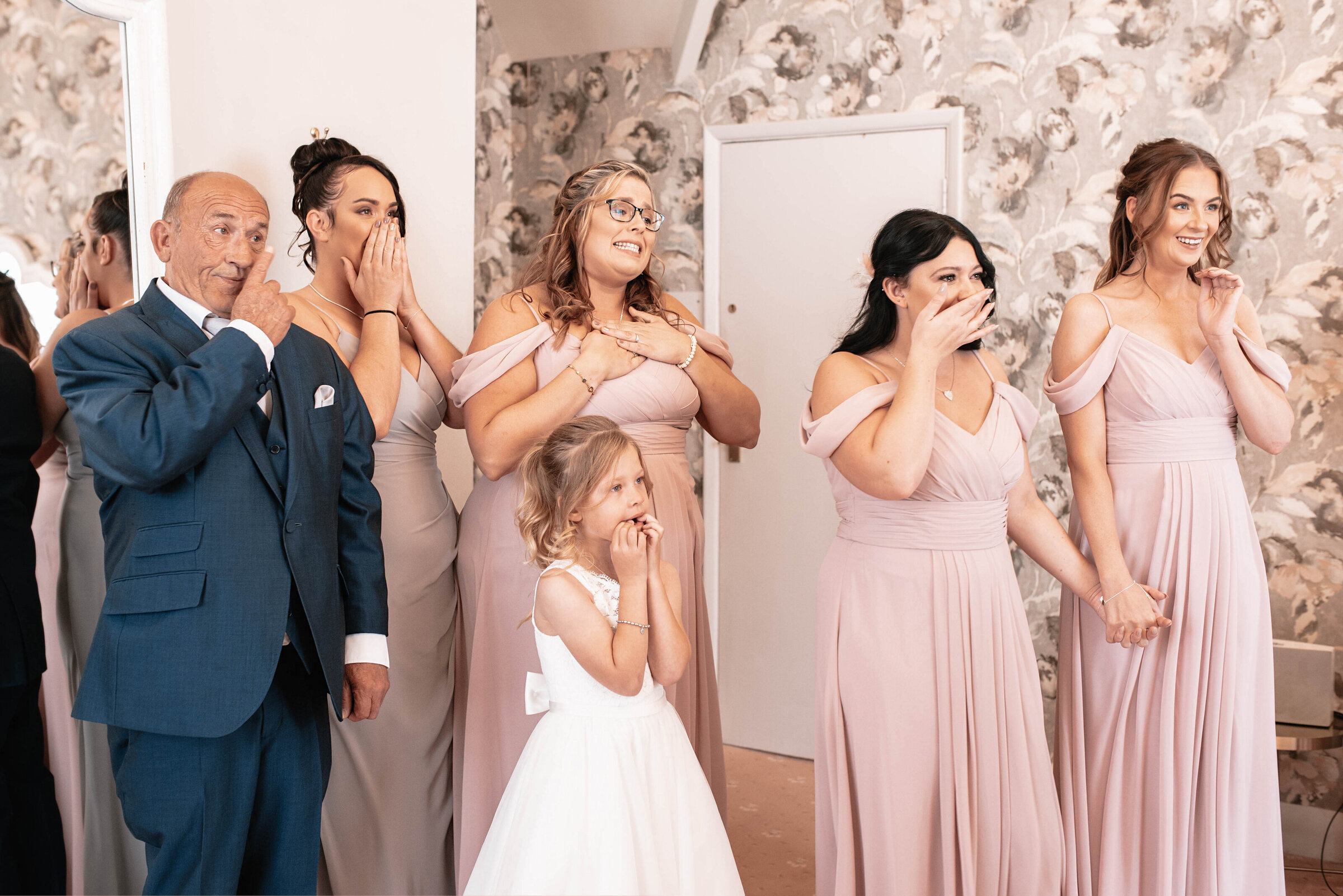 Five bridesmaids and father of the bride smiling and crying happy tears at first look of bride in her wedding dress