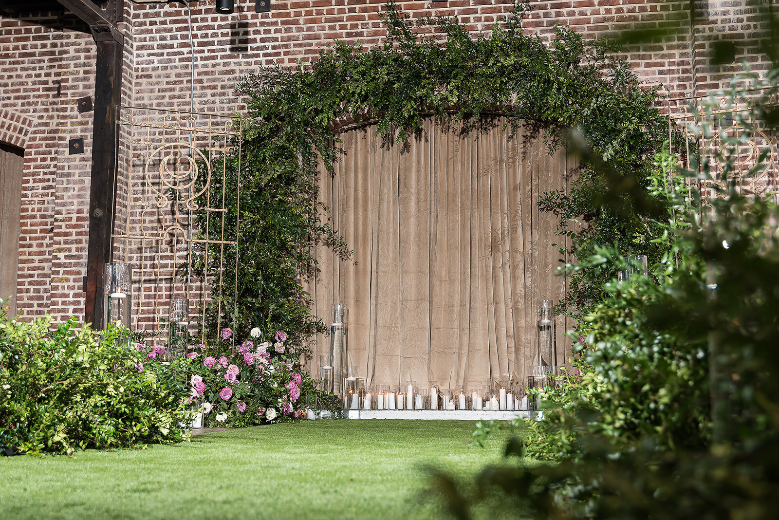 Floral altar arch with soft blush and lavender roses, textured greenery, and candles in front of taupe draping at The Kent Memphis wedding, styled by Wells Design Co.