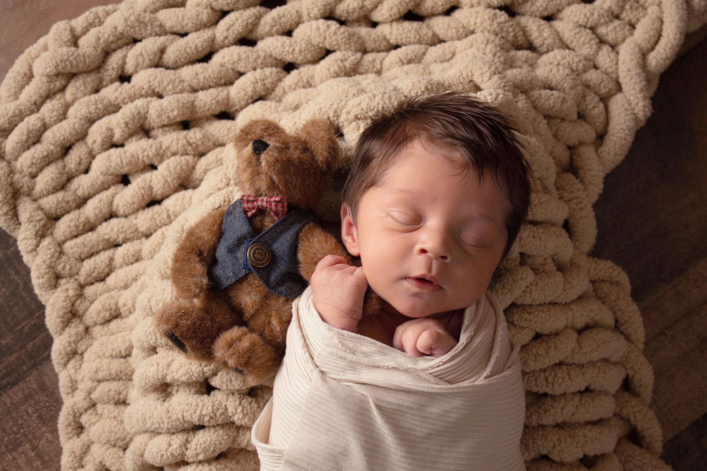 Minot AFB newborn wrapped while holding his teddy bear's hand in his.
