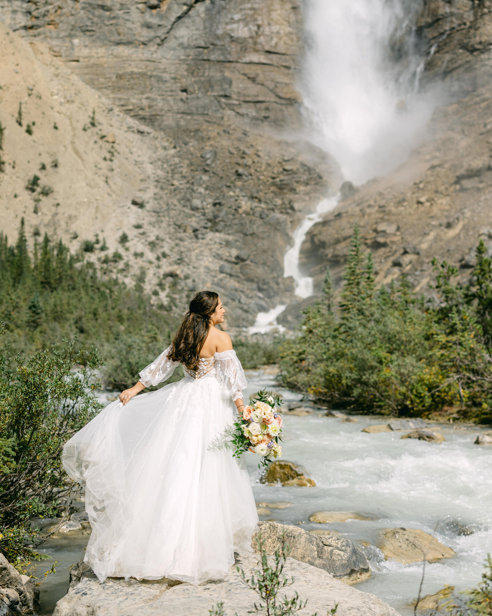 A breathtaking moment as the bride twirls and plays with her dress, standing before a powerful waterfall in Yoho National Park. The cascading water creates a dramatic and awe-inspiring backdrop, capturing the beauty, movement, and magic of her unforgettable wedding day in the heart of the Canadian Rockies.