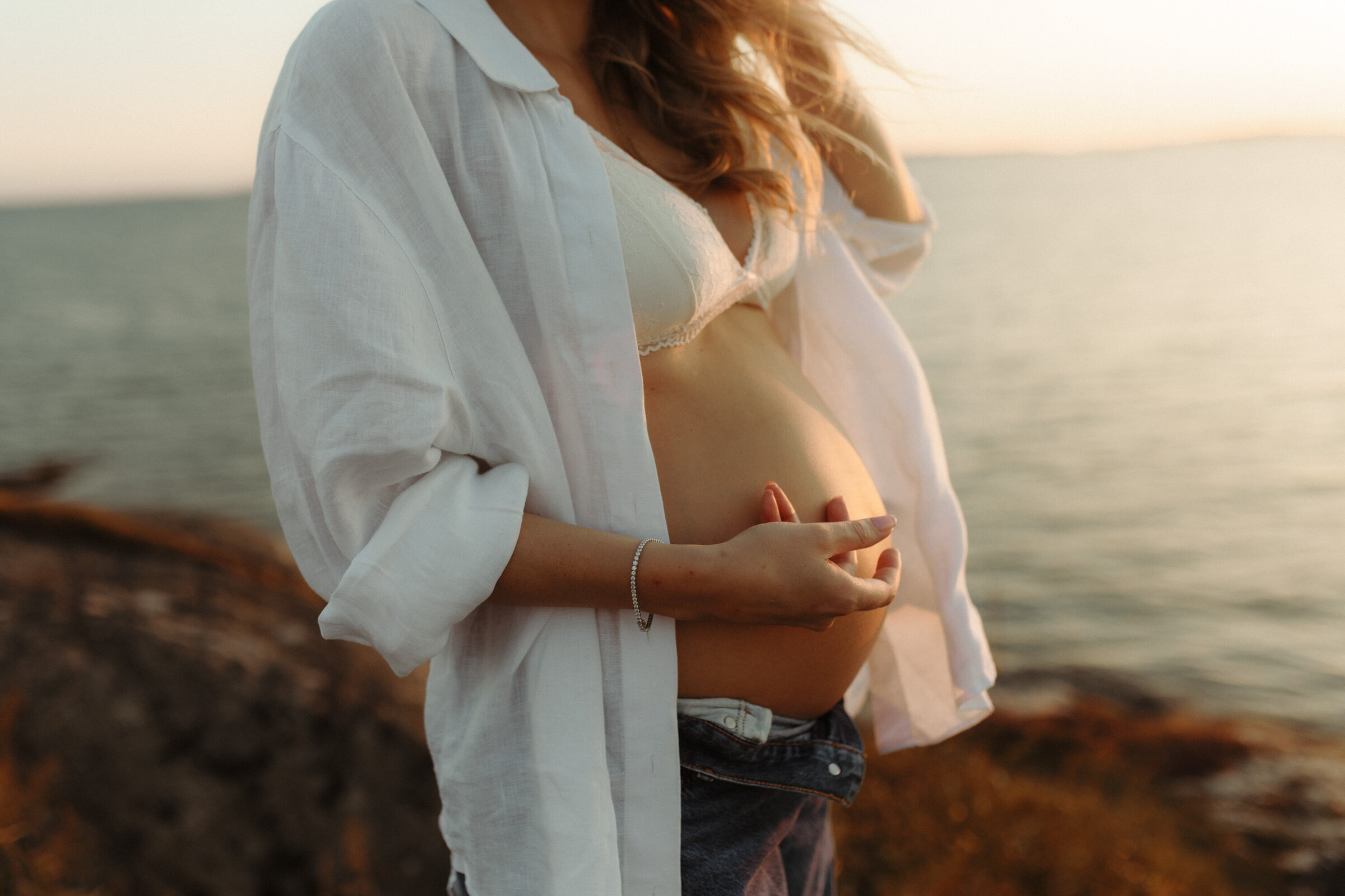 en gravid kvinna med vit skjorta och jeans smeker sin mage