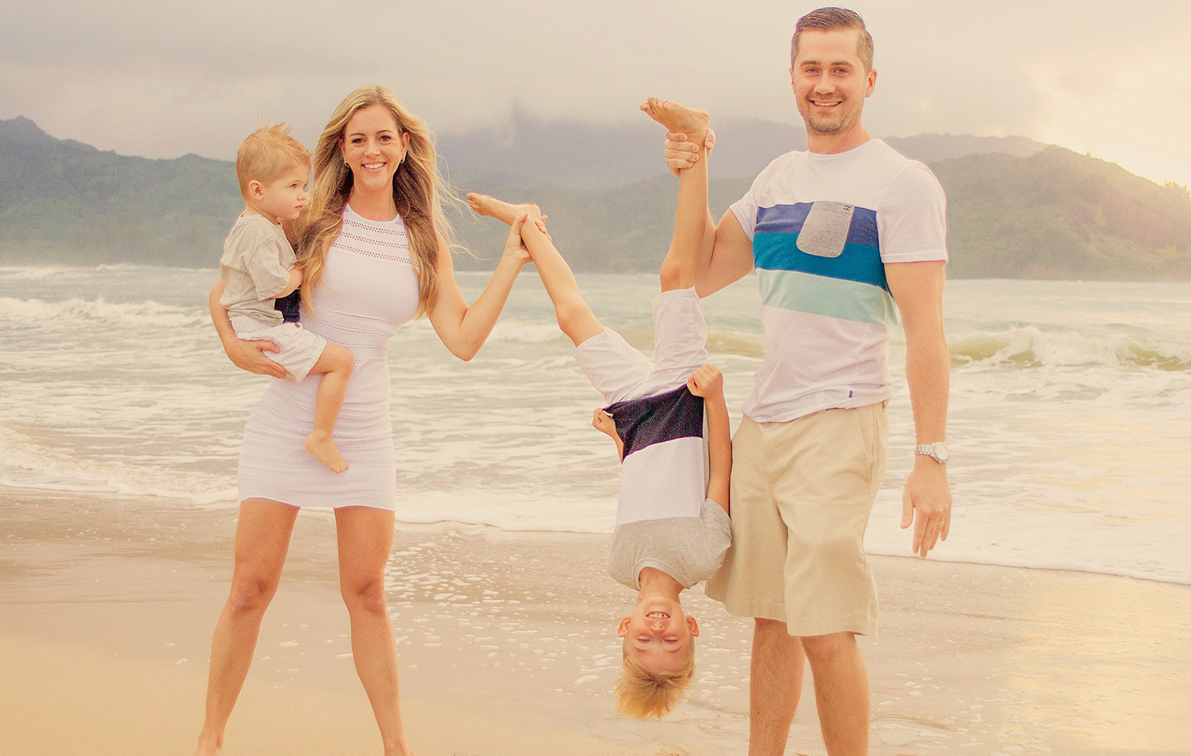 Family on the beach holding their son upside down.