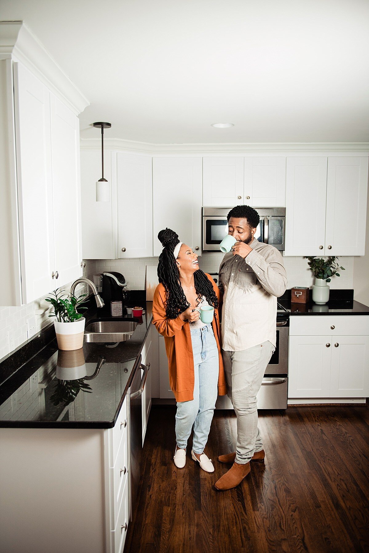 Couple standing in white, grey and black kitchen drinking coffee together.