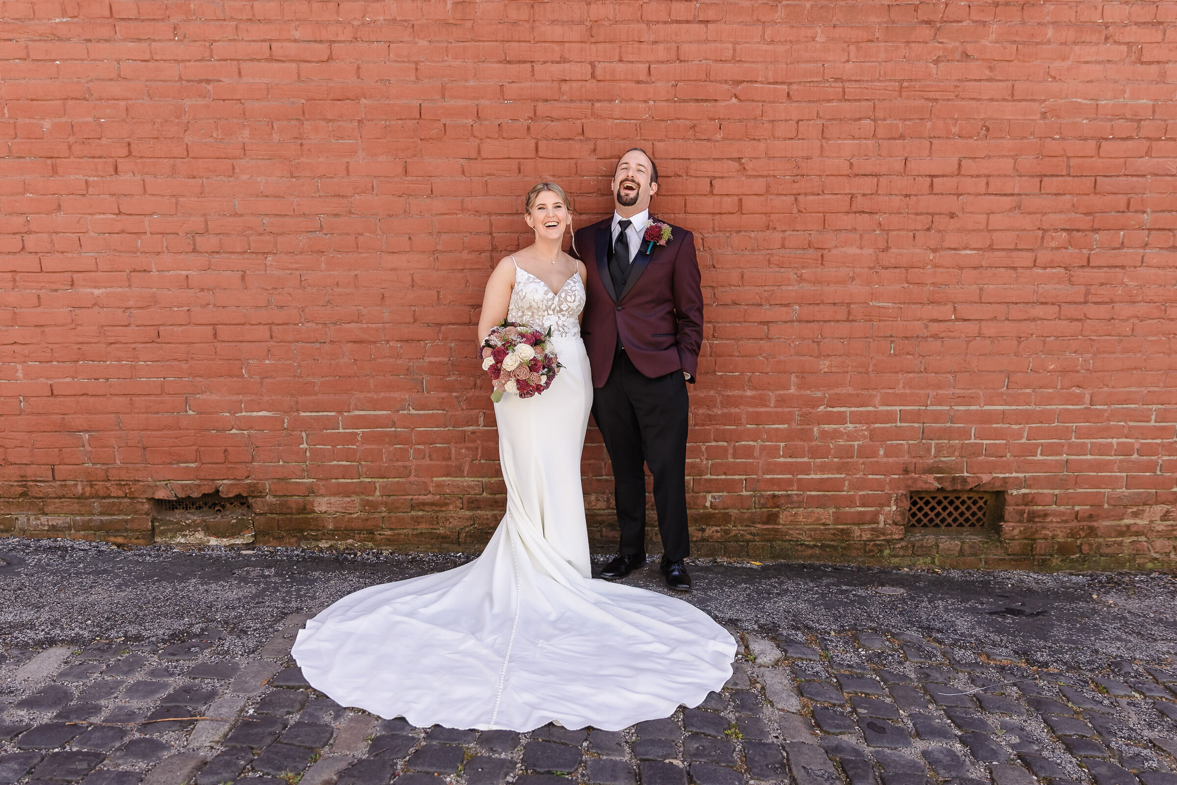 "Bride and groom share a huge laugh against the brick wall at 128 South in downtown Wilmington"