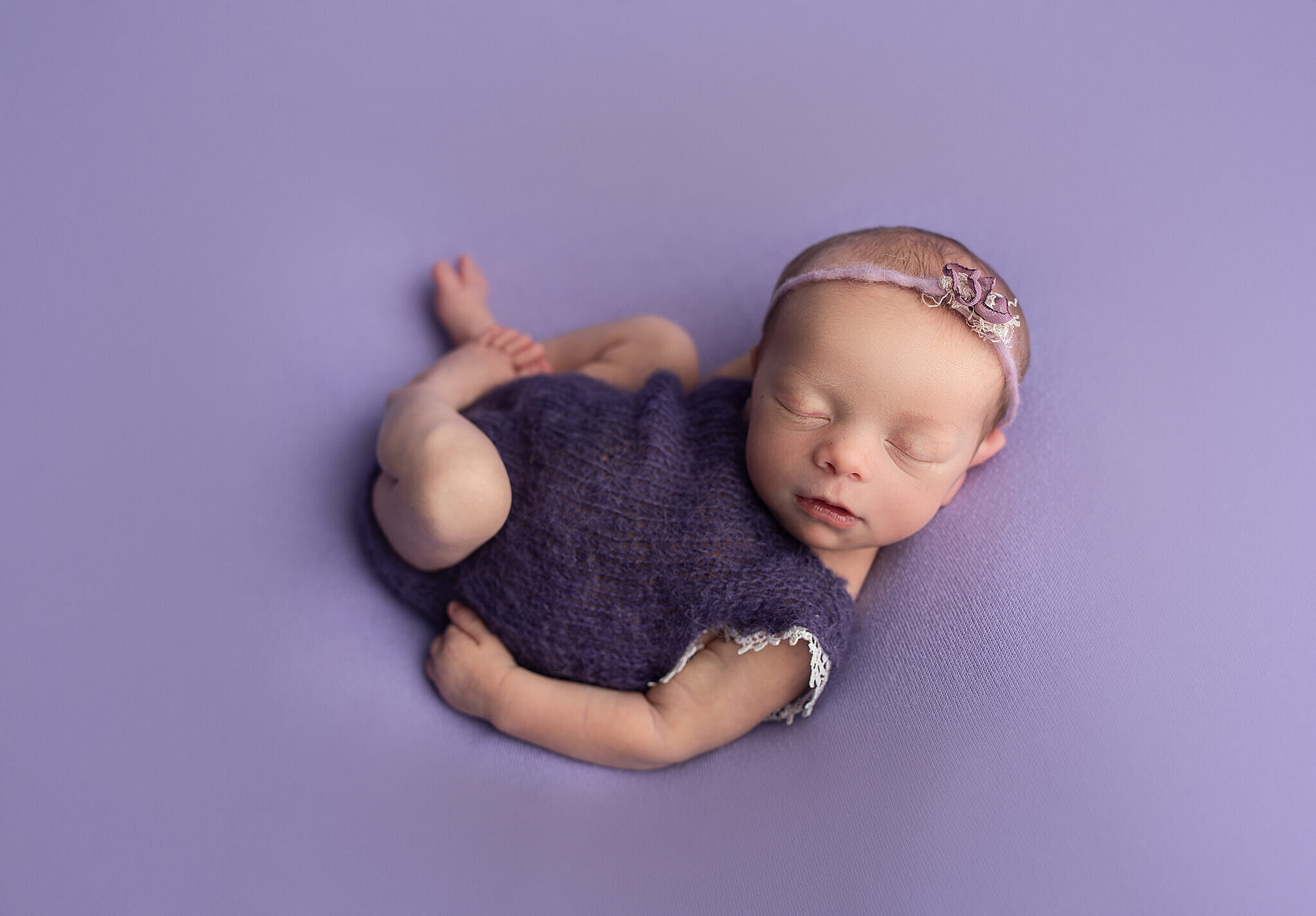 newborn baby girl laying on a purple blanket in a cute purple outfit