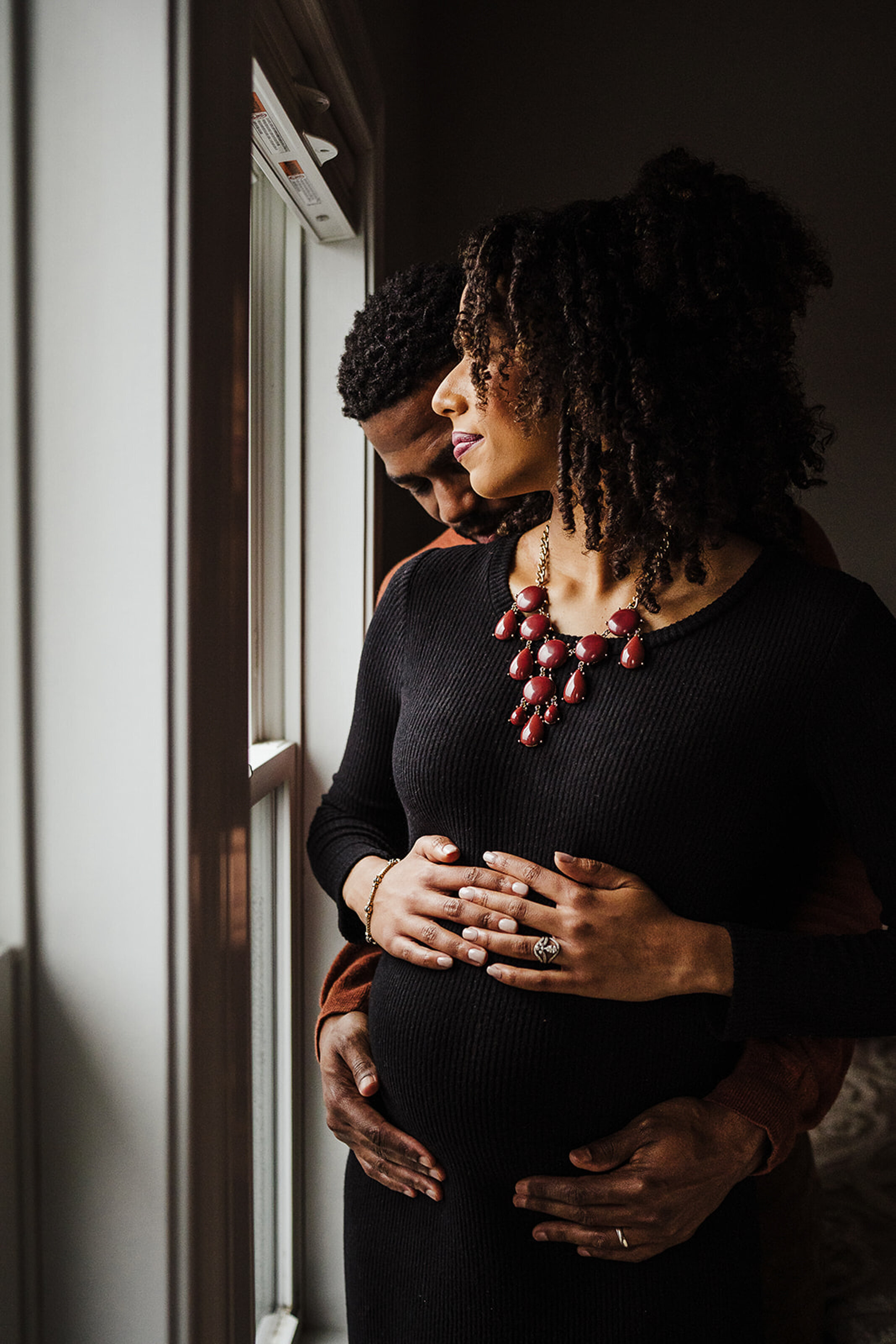 pregnant couple snuggles by window during in-home maternity session in boston