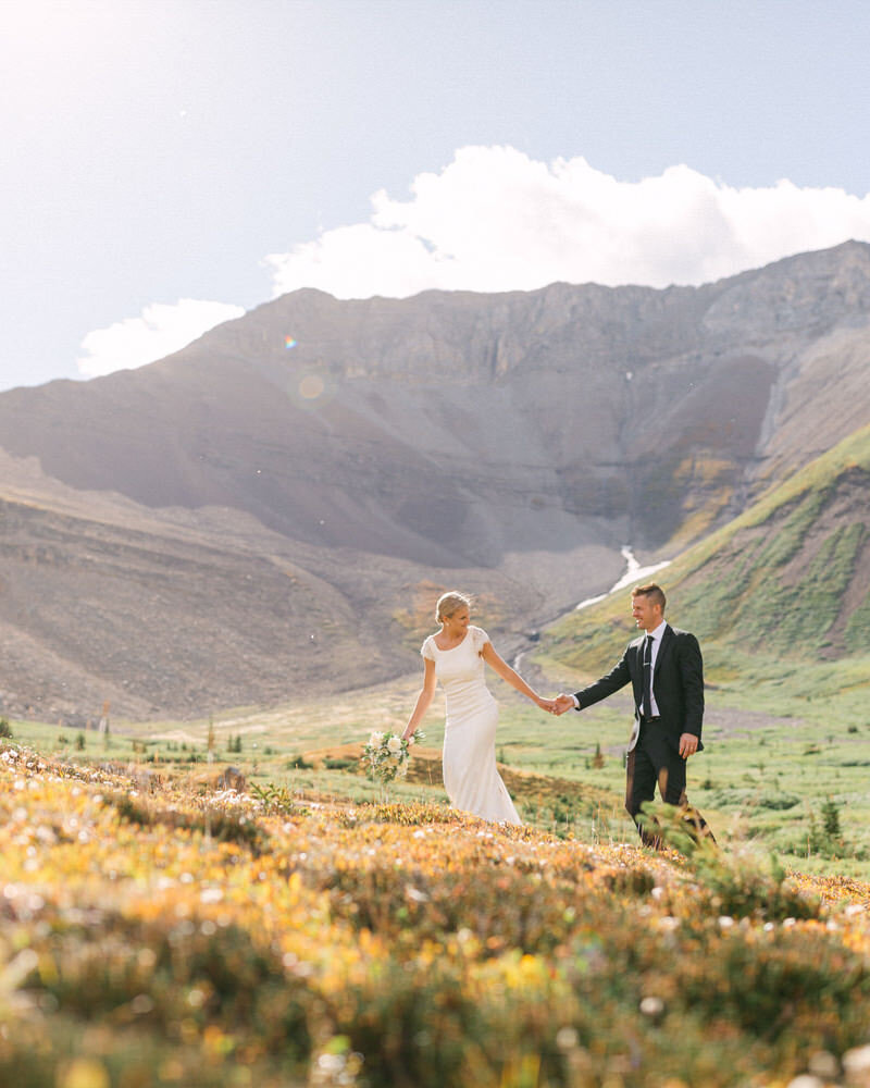 A breathtaking elopement photograph of the bride and groom walking together near Mount Charles Stewart in Banff National Park. Captured on a gorgeous summer day, this warm and radiant moment showcases the couple’s love amidst the stunning mountain backdrop, embracing the beauty and serenity of the Canadian Rockies.