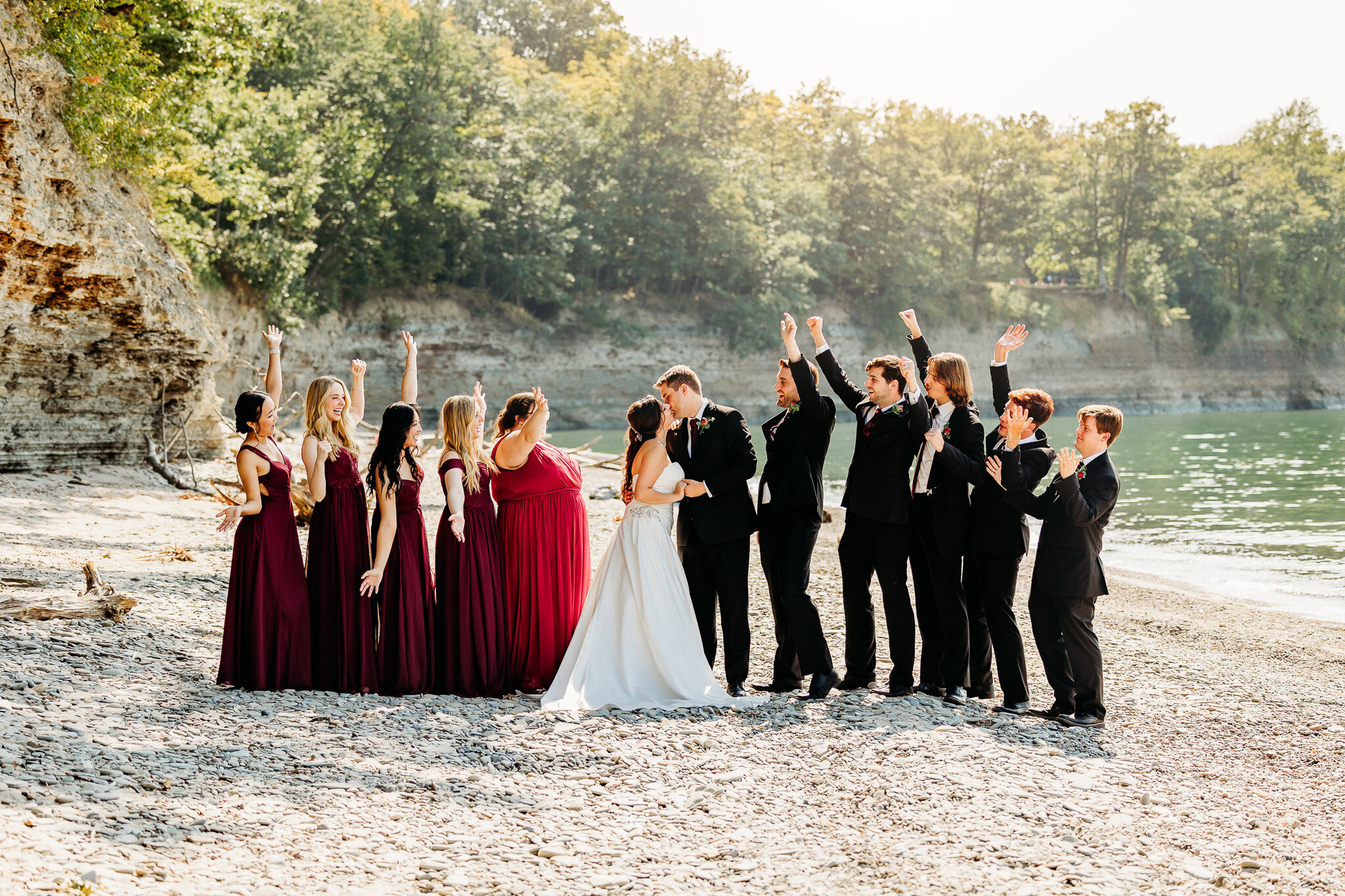 Bridal party cheers a kiss between the bride and groom on a beach 