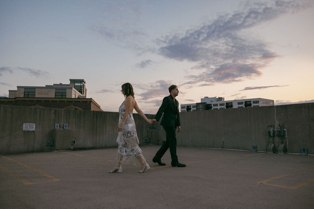 Sunset rooftop engagement photo session with bride and groom holding hands starting to walk away from eachother in opposite directions