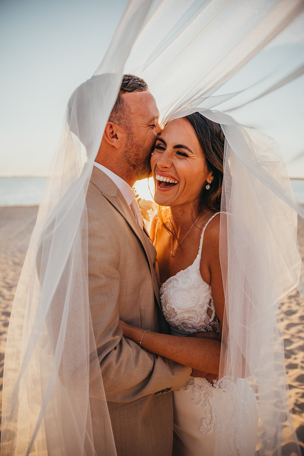 bride laughs with her husband under veil