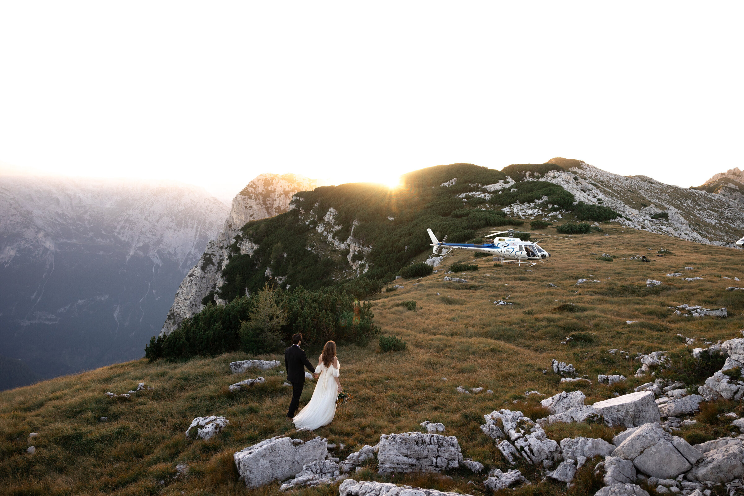 A couple walking towards a helicopter on top of a cliff in the dolomites. Photo taken by Kollar Photography, Arizona Elopement Photographer. 