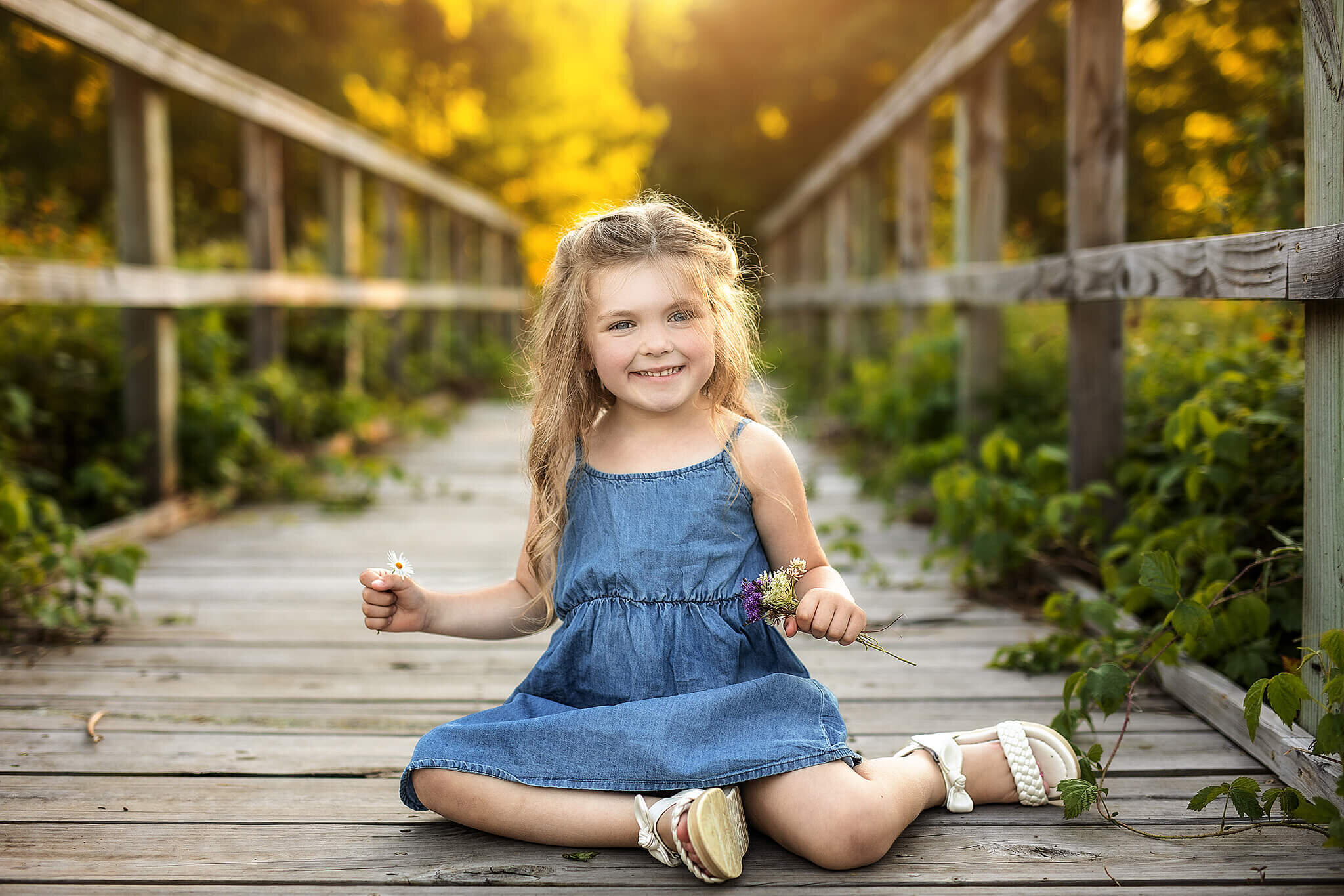 4 year old girl sitting on a bridge smiling big while holding flowers