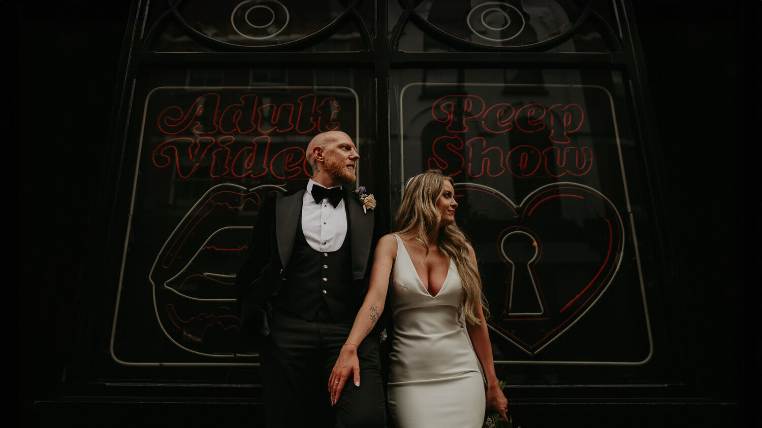 Bride and Groom stand outside the Peep Show Neon in Soho on their wedding day.