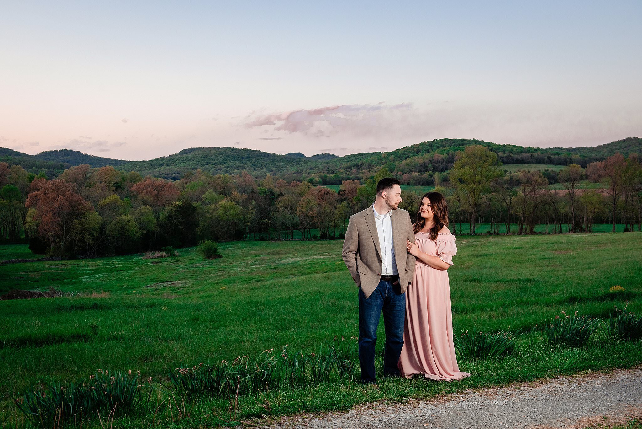 Landscape photo of rolling hills and open green field with engaged couple standing in the forefront