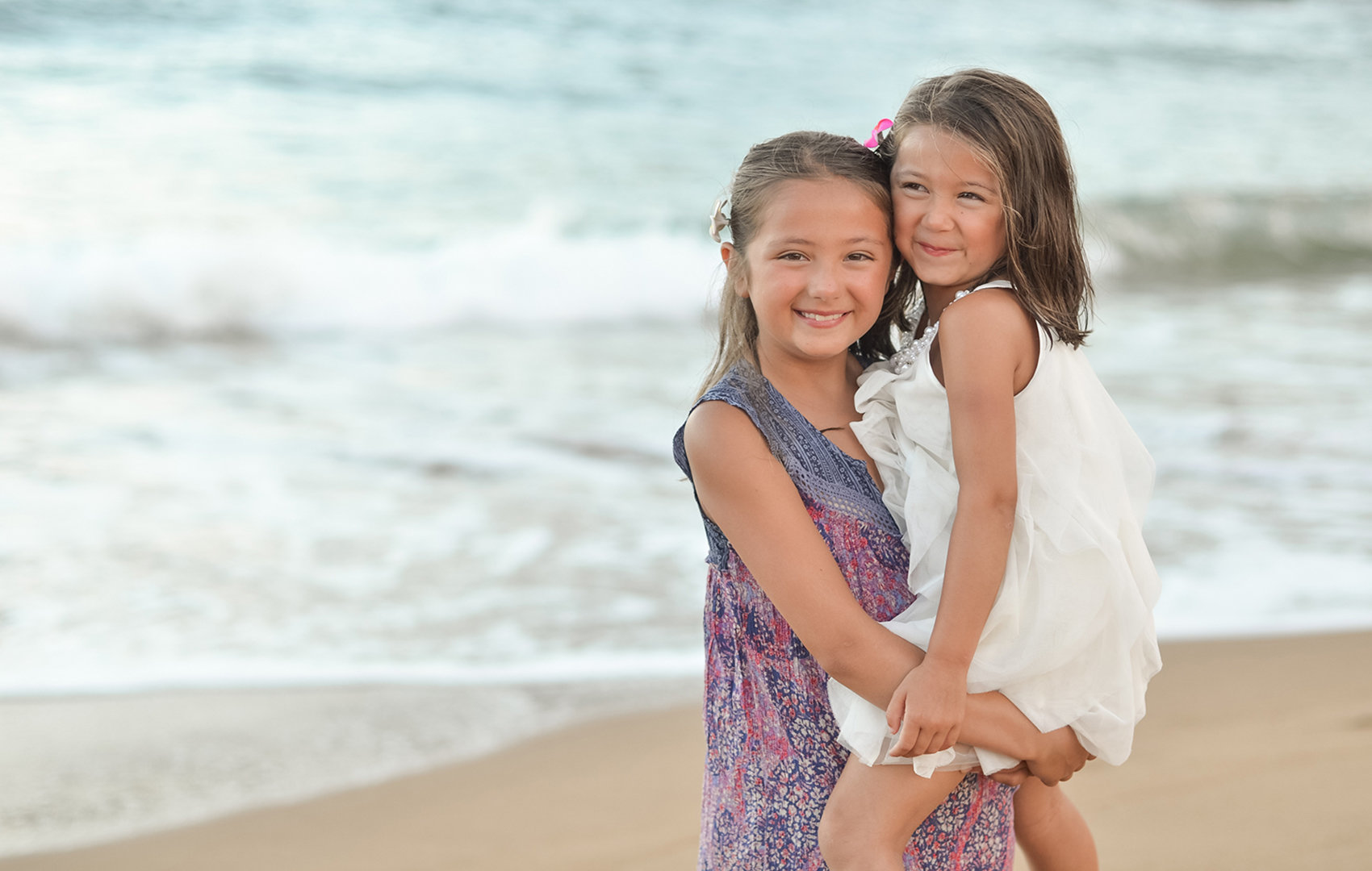 Big sister hold little sister on the beach in Kauai for their family portrait session.