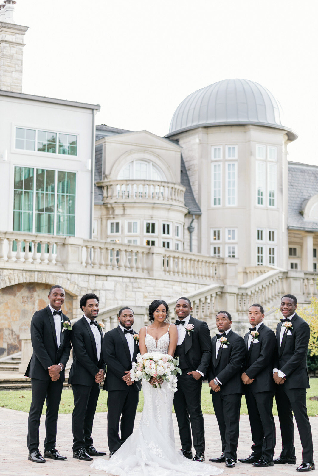 Formal wedding portrait of Nadia and Norman with the groomsmen, with The Olana venue in the background.