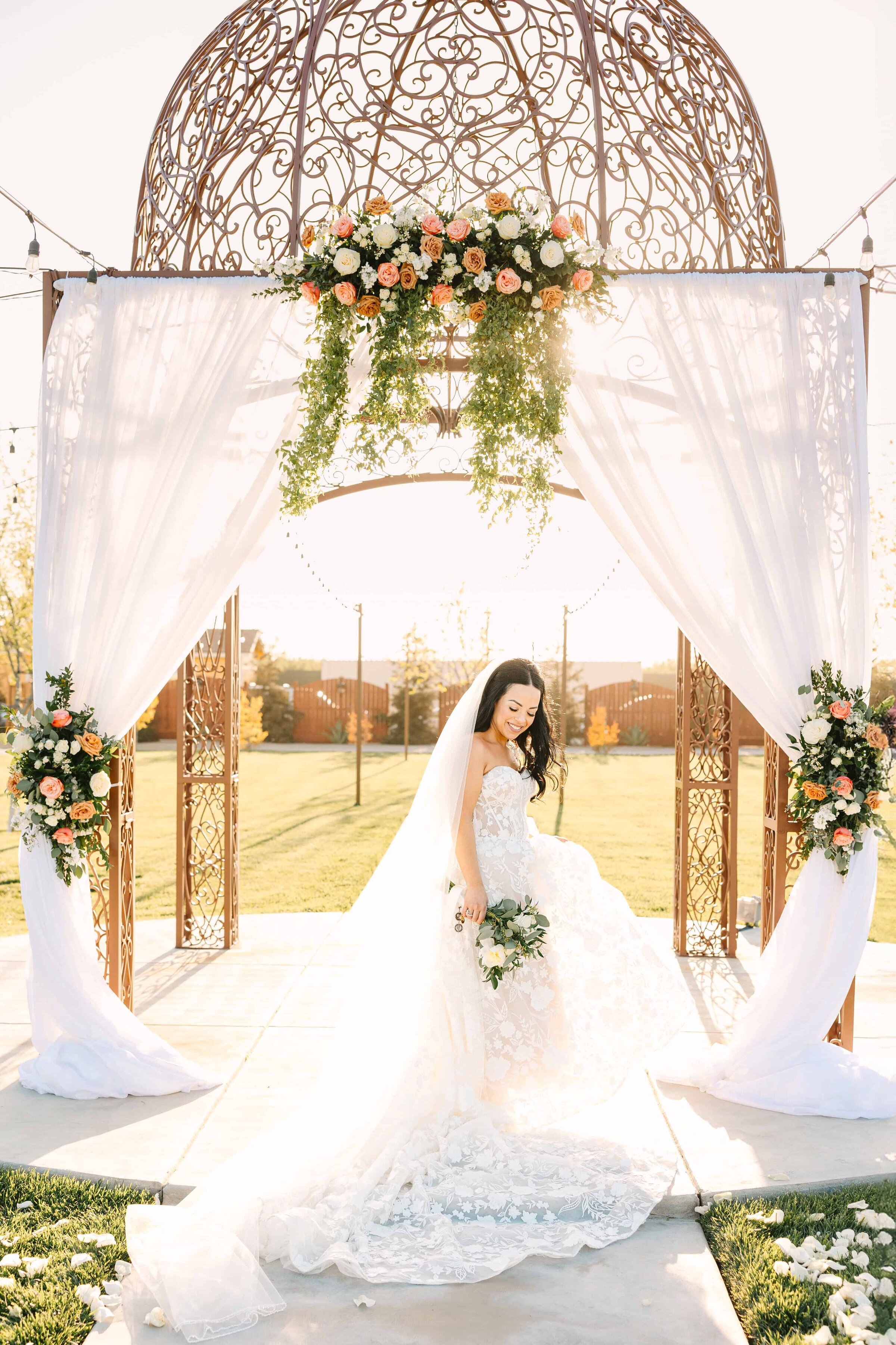 Bride dances and swishes her dress around in the sunlight under her wedding arch