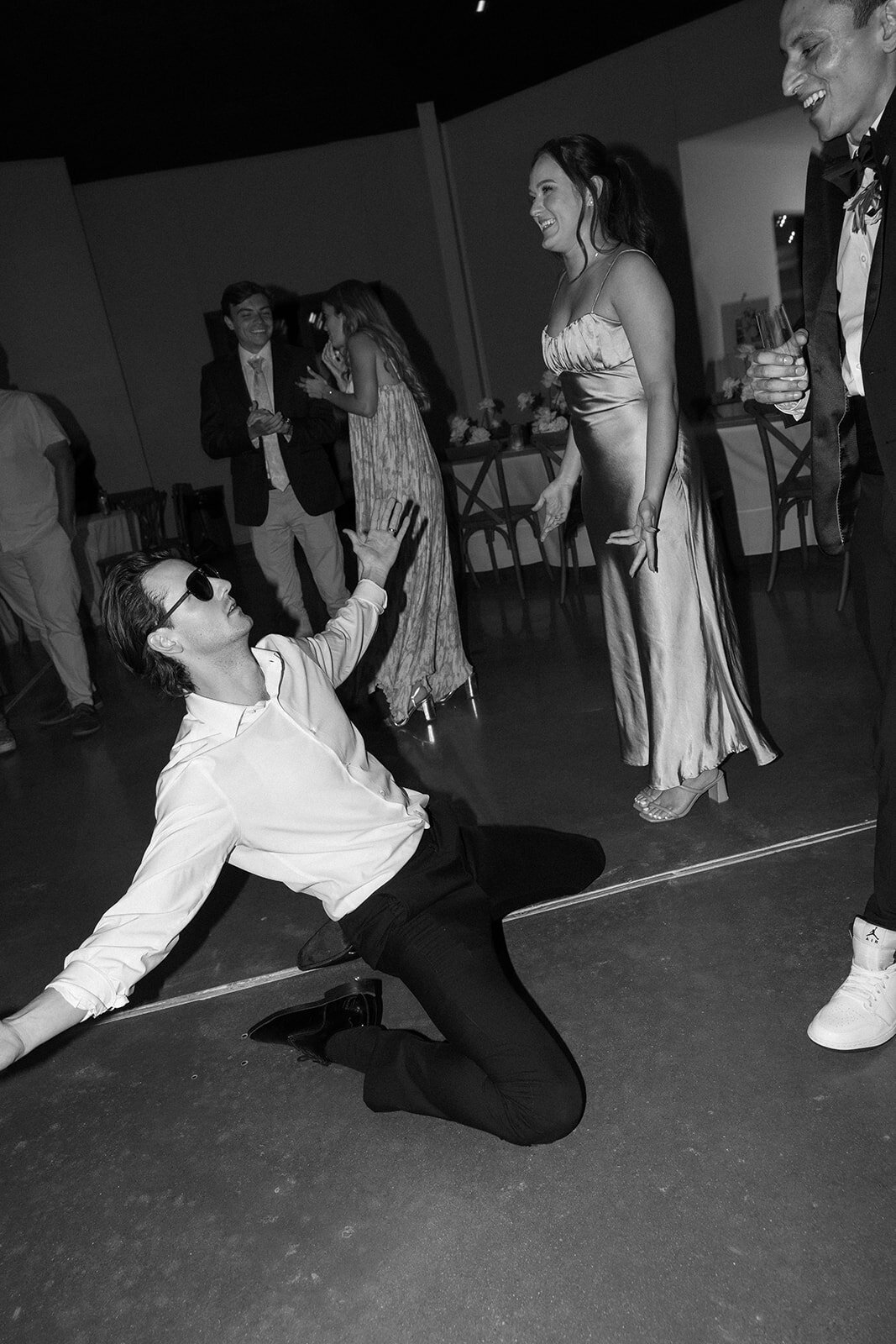 A guest in sunglasses sliding on the floor during dancing at the reception. 
