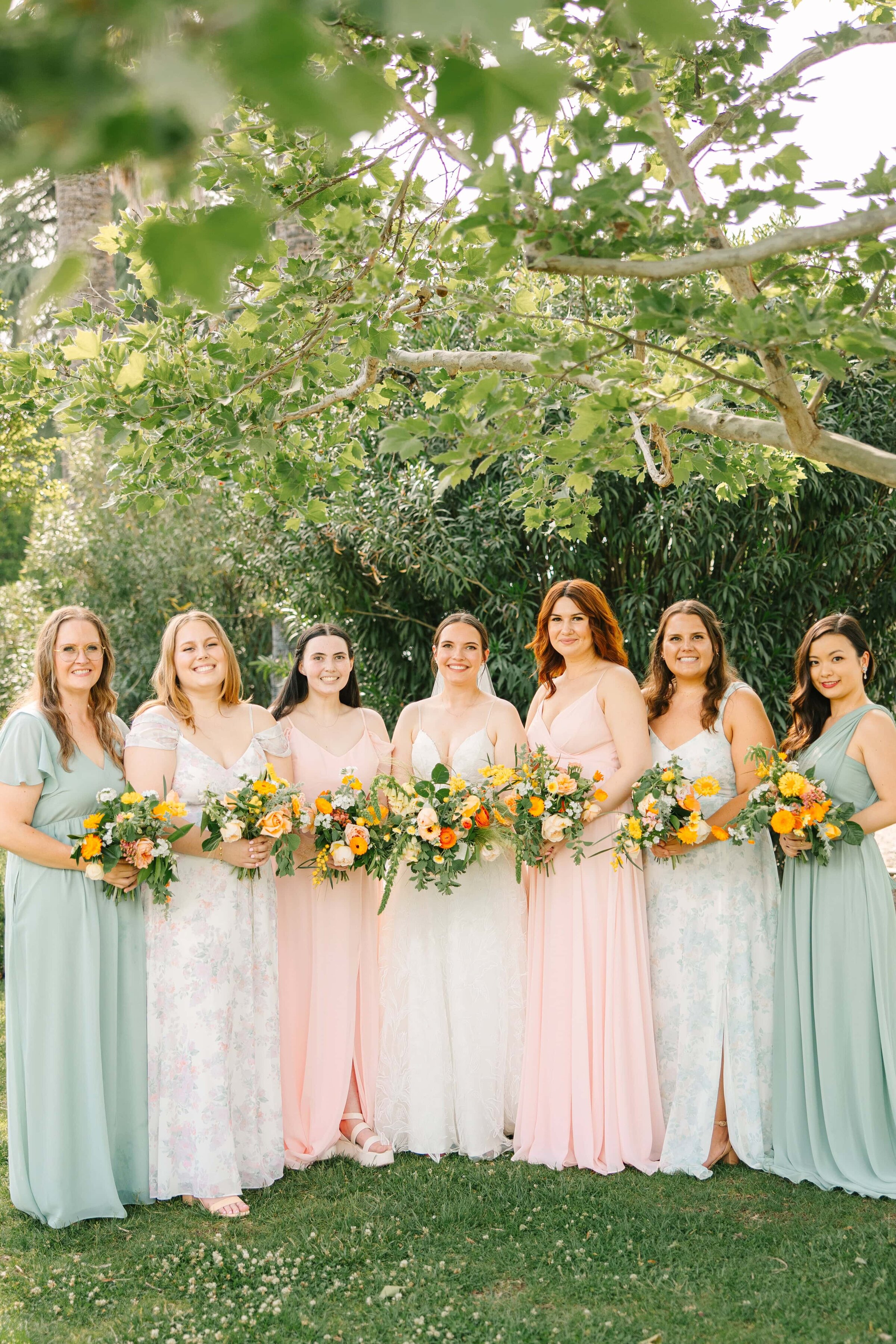 bride and her garden part bridesmaids smile at the camera holding her bouquet