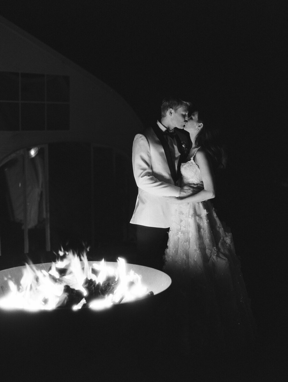 bride and groom kissing by a fire pit at night